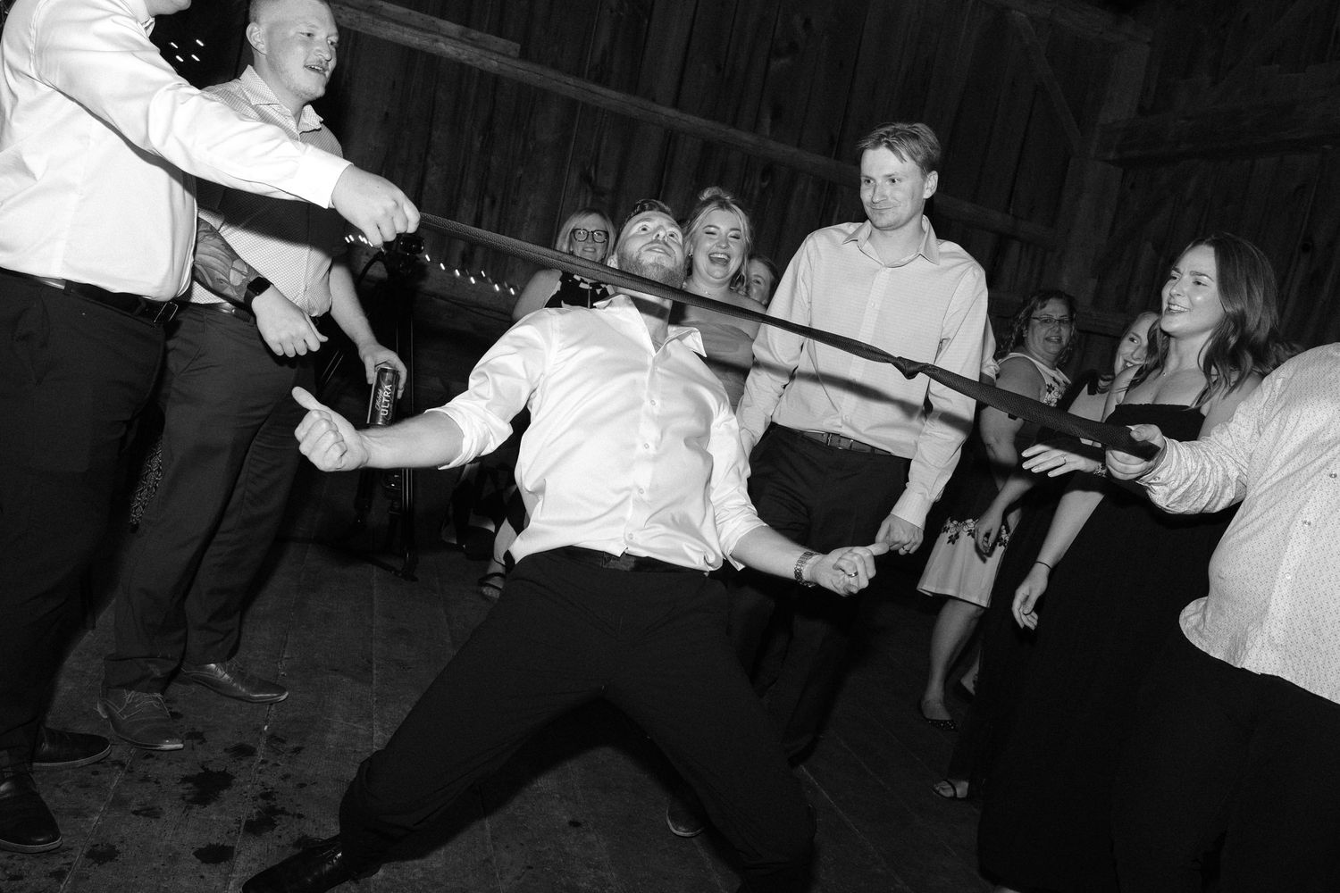 Wedding guests doing limbo dance under a tie during fun barn reception dance floor celebration.