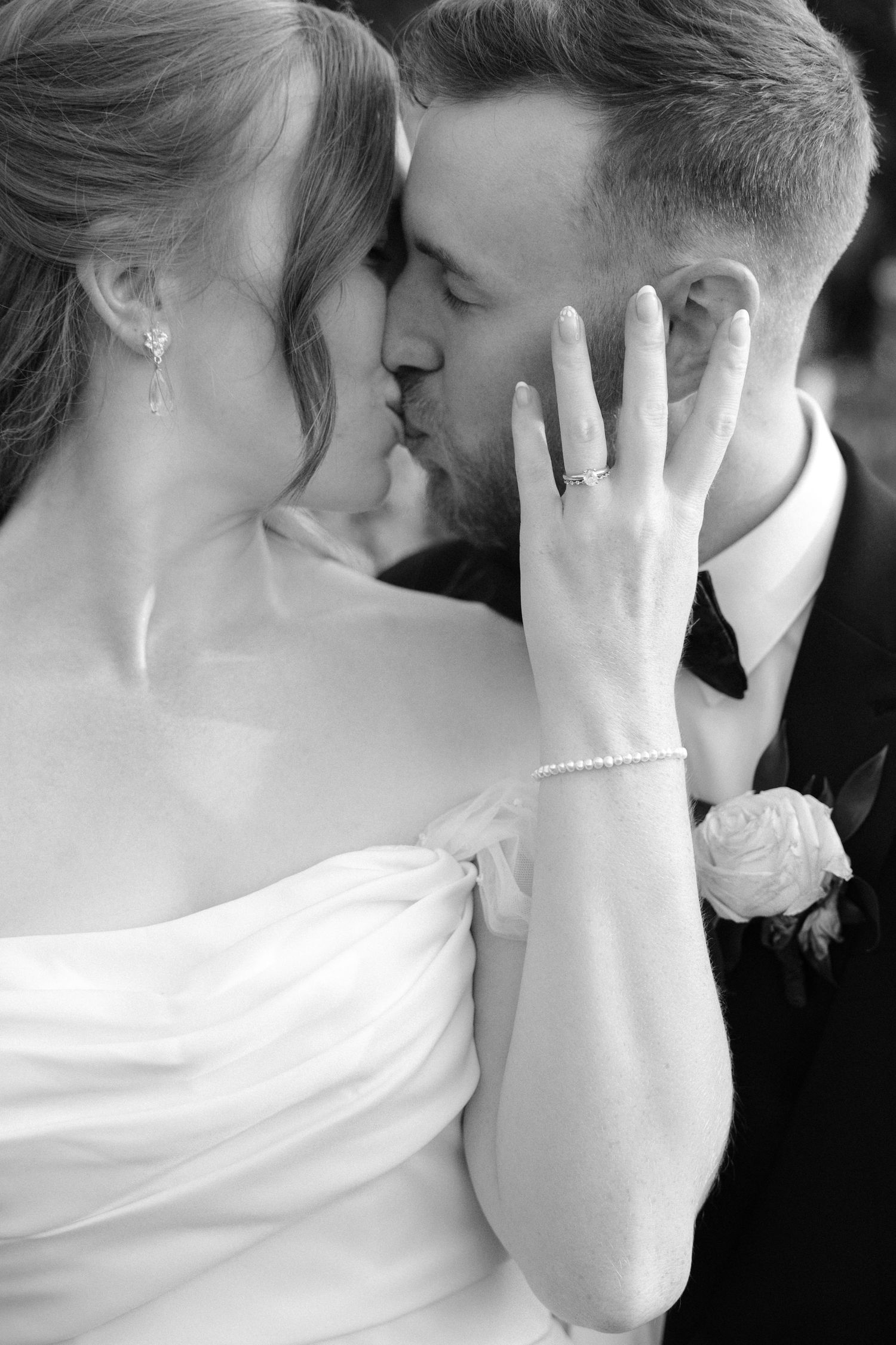 Black and white close-up of bride and groom kissing while bride displays her diamond engagement ring.