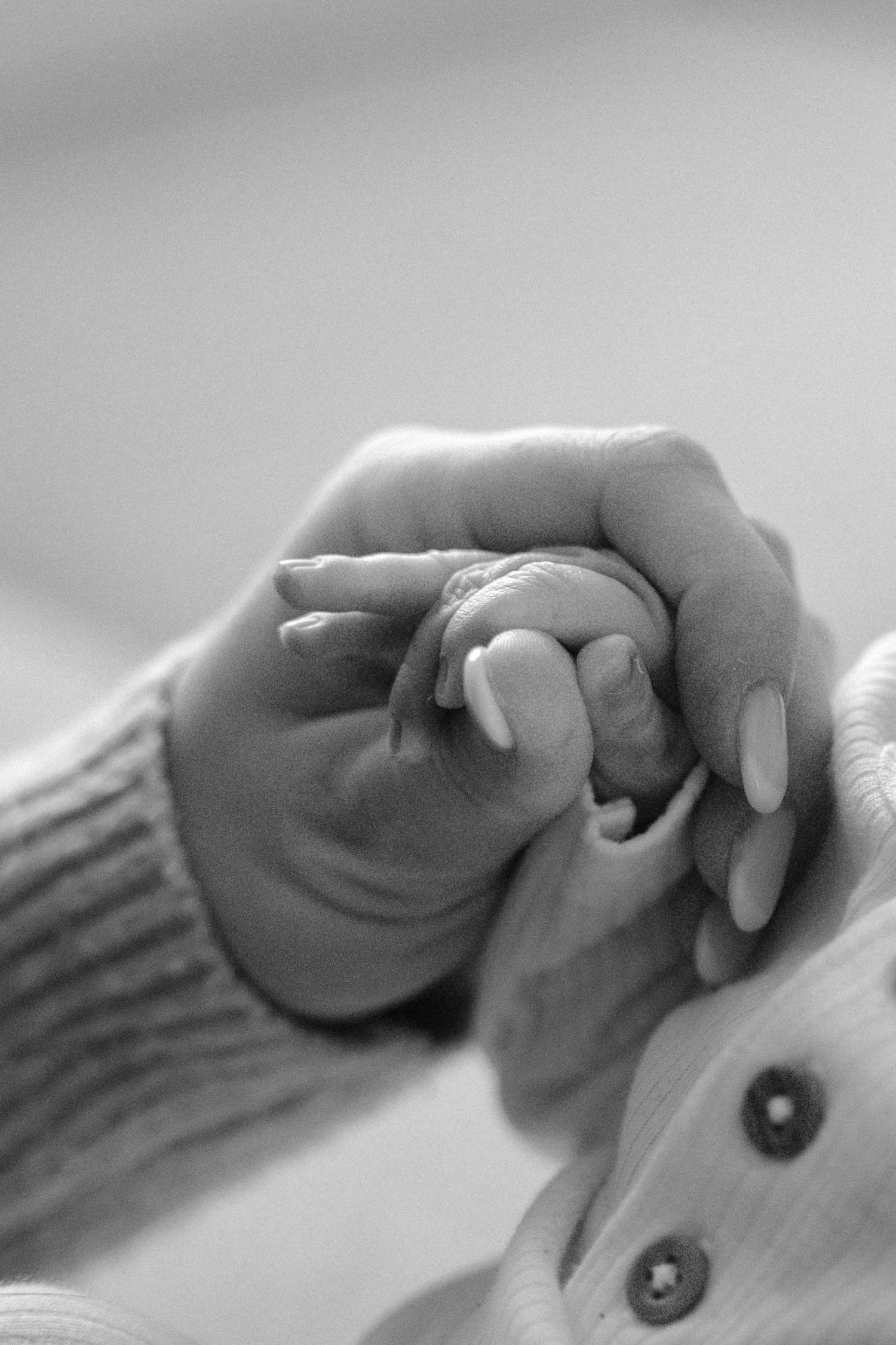 Black and white close-up of a mothers hands gently holding her newborns tiny hand in a tender moment.