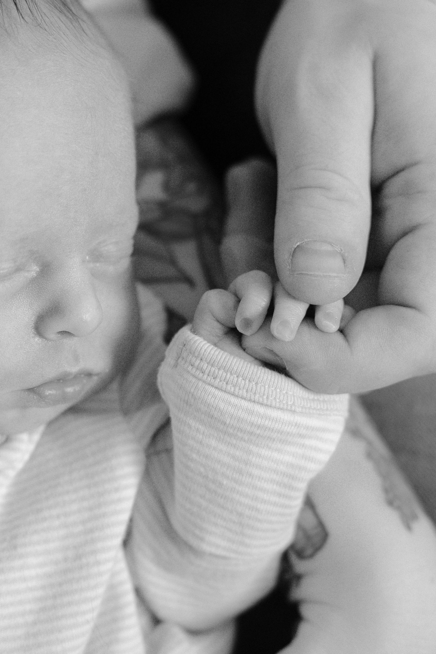 Black and white close-up of a sleeping newborn baby gently gripping an adults finger.