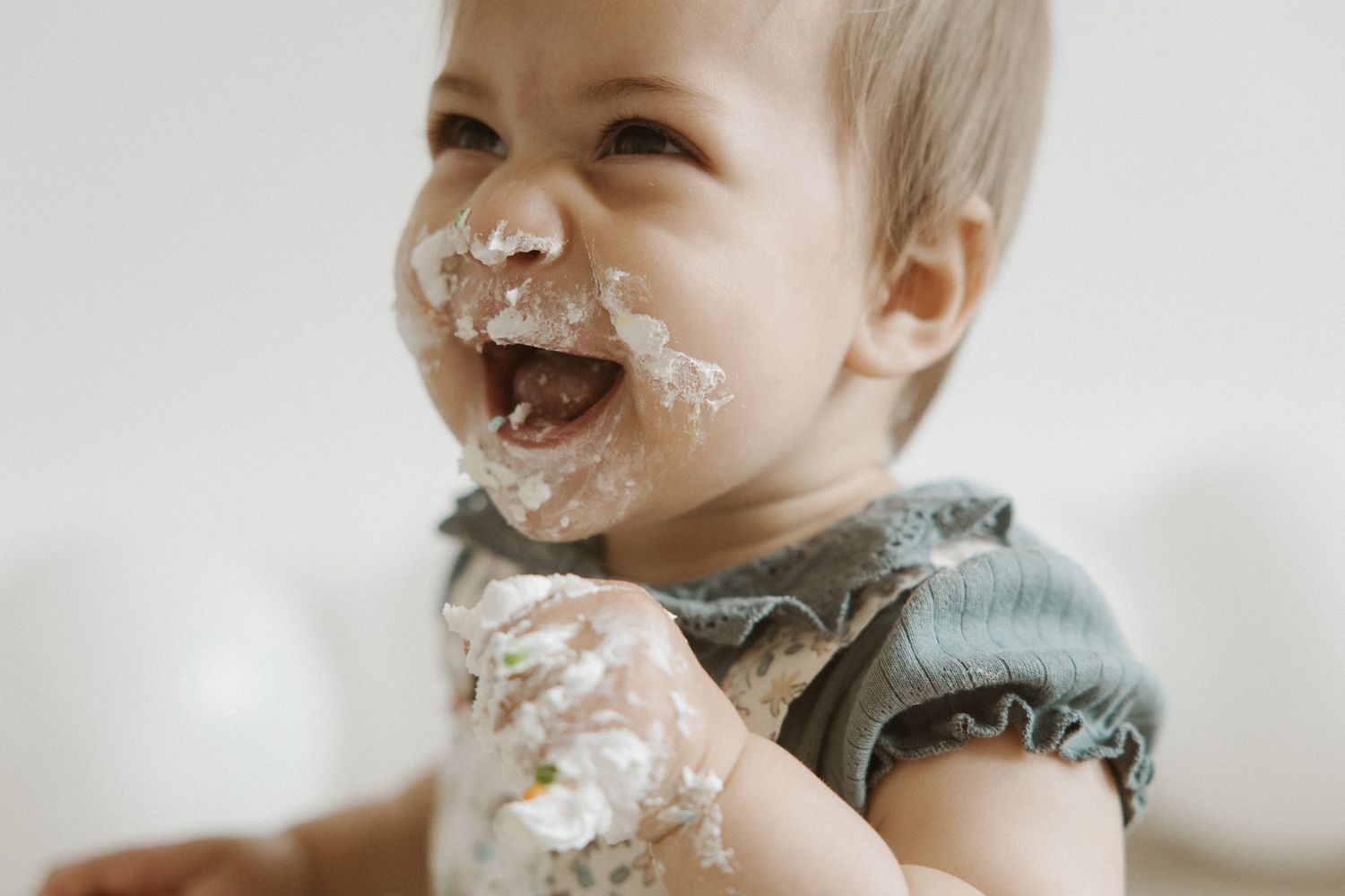 Adorable laughing baby with cake smeared on face and hands during first birthday smash.
