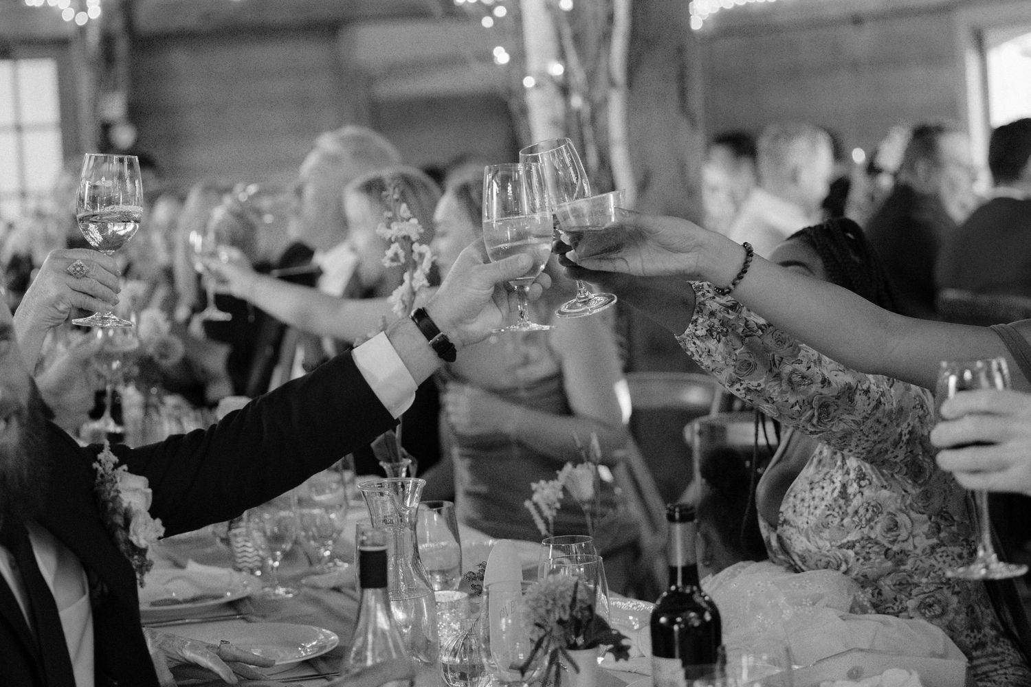 Wedding guests raise champagne glasses in a toast at a rustic barn reception.