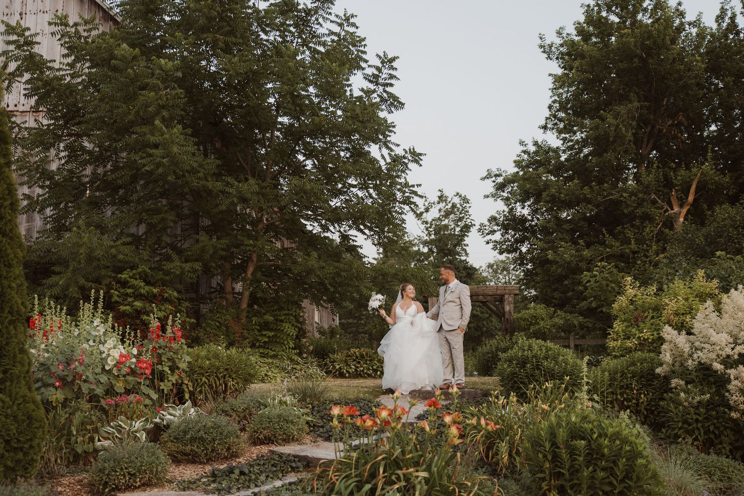 Bride and groom share a romantic moment surrounded by lush garden blooms at outdoor wedding venue.