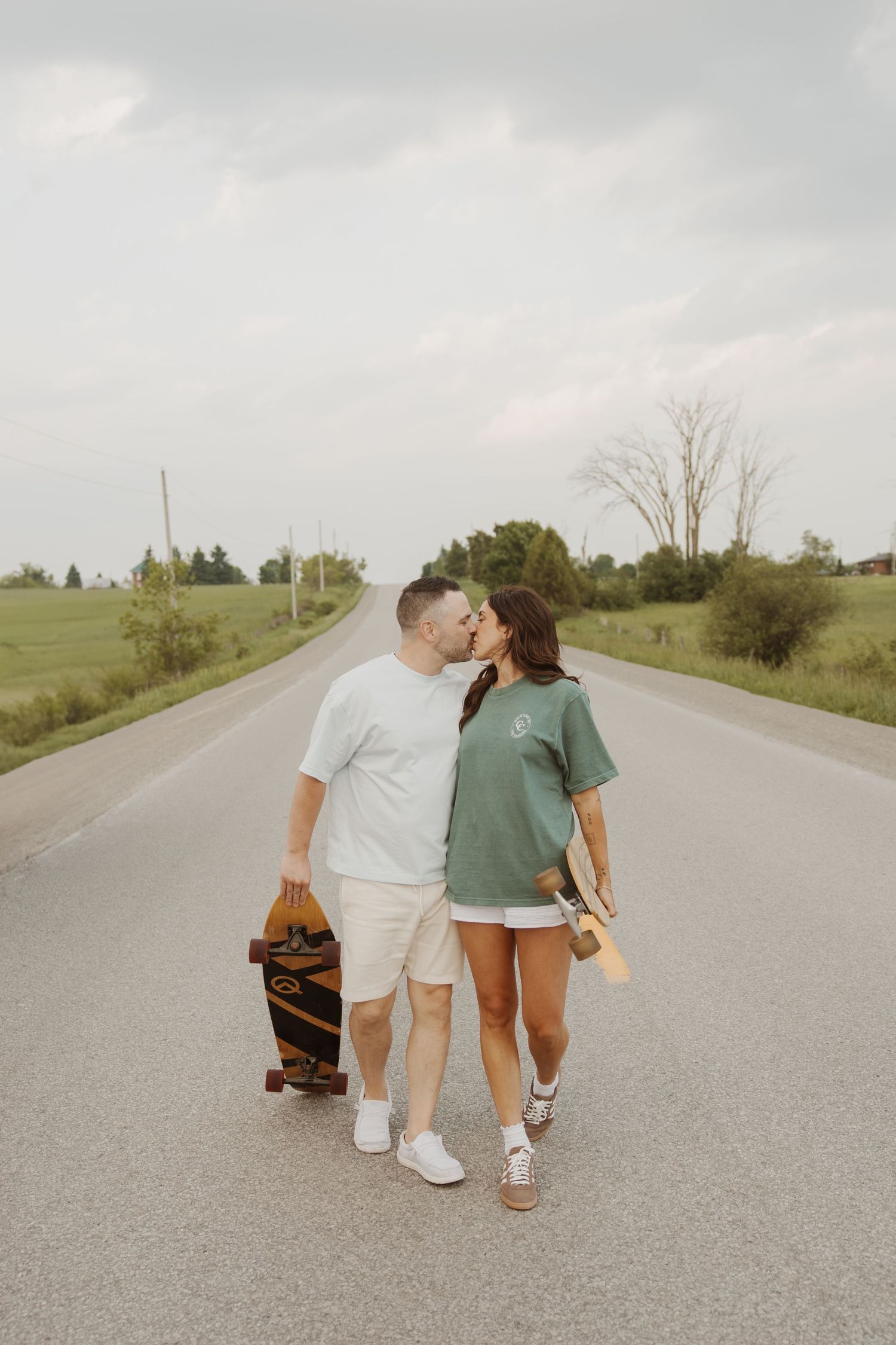 Couple kissing while walking on country road carrying longboard skateboards.