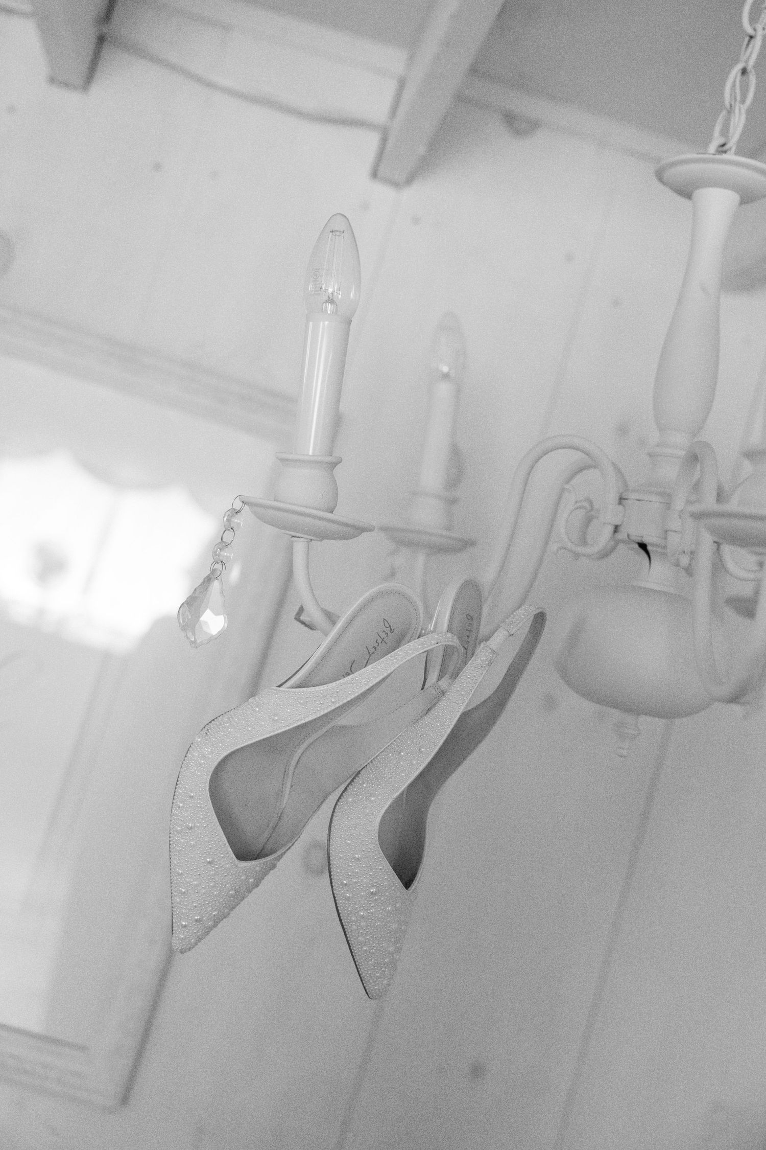Black and white photo of bridal heels hanging elegantly from a white chandelier.