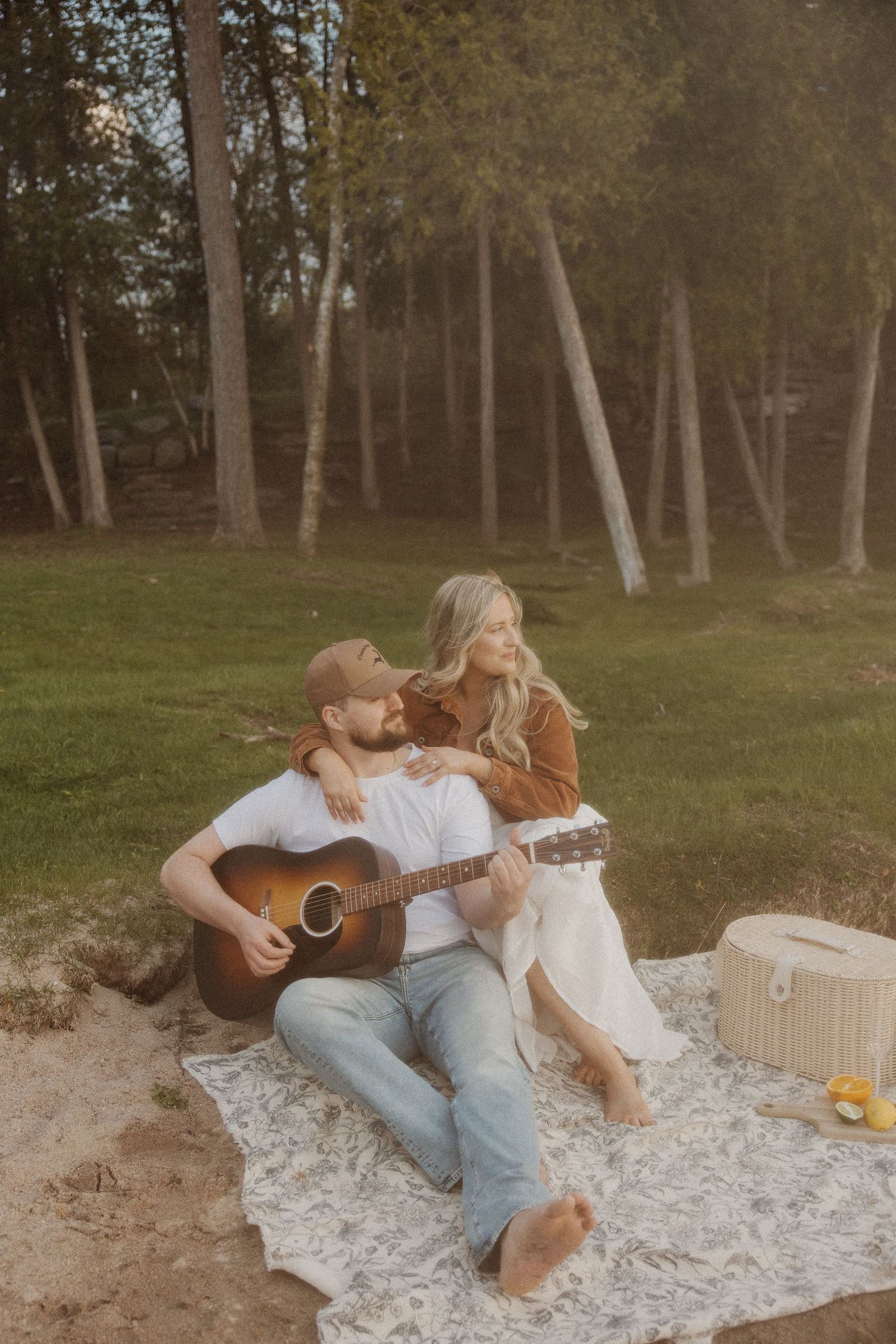 Couple relaxing on blanket outdoors with acoustic guitar and picnic basket.
