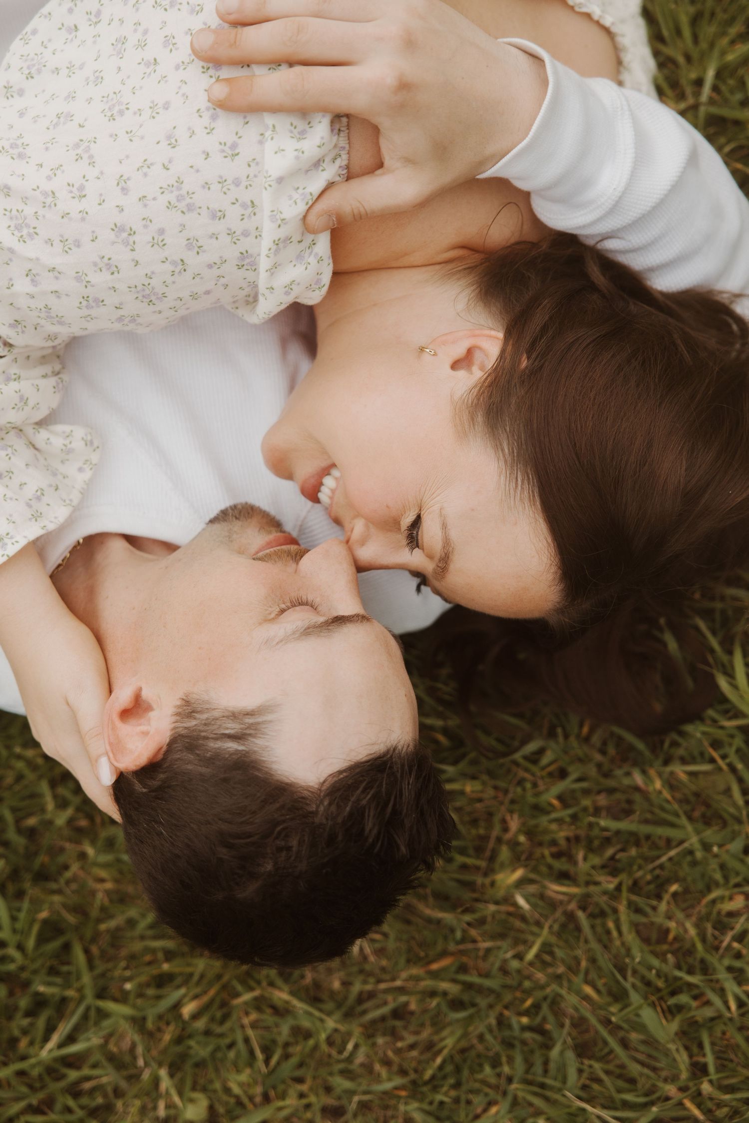 Couple lying on grass touching foreheads and smiling intimately.