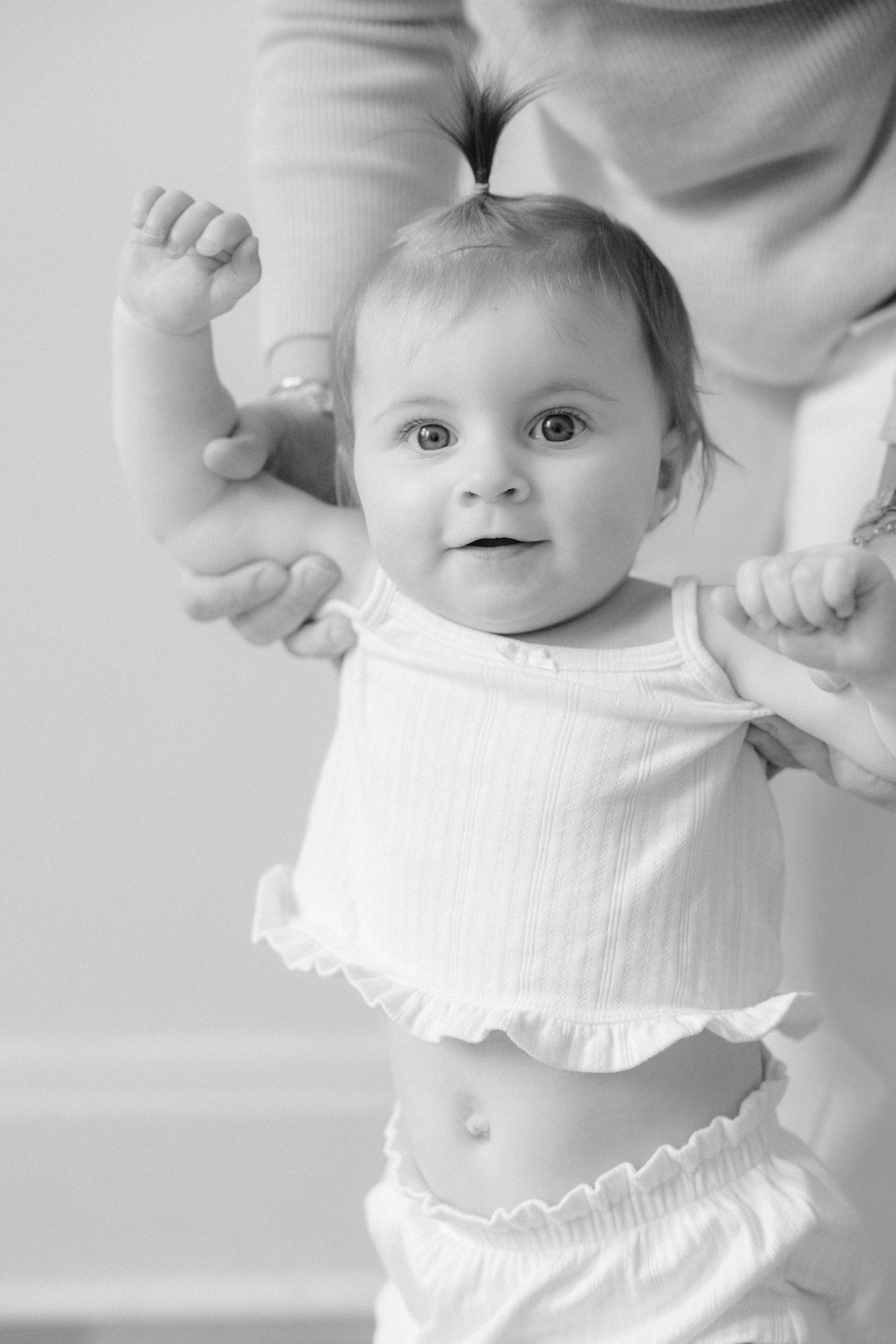 Black and white portrait of a smiling baby being held up by an adult in a bright studio setting.