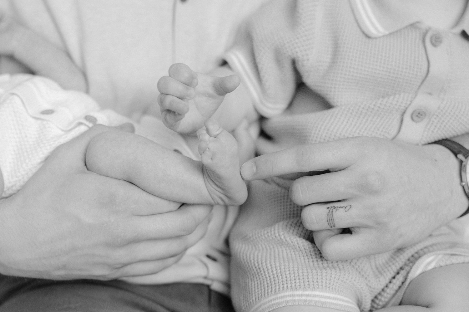 Black and white close-up of parents holding their newborn baby's tiny feet and hands.