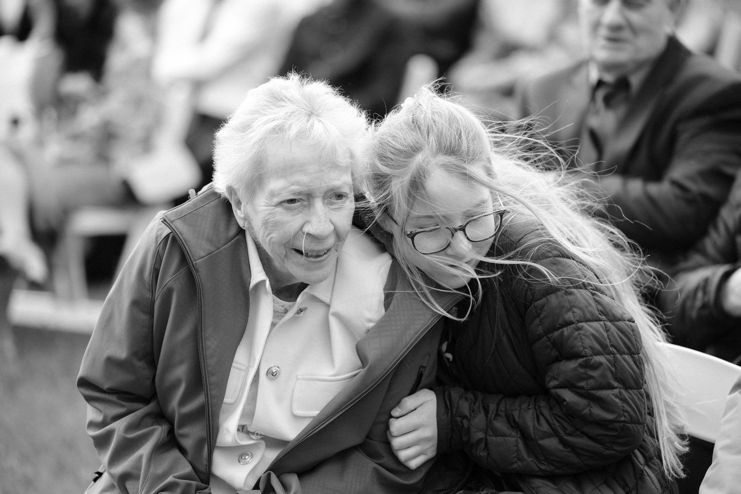 Black and white photo of elderly woman and younger woman sharing a warm embrace at outdoor wedding ceremony.