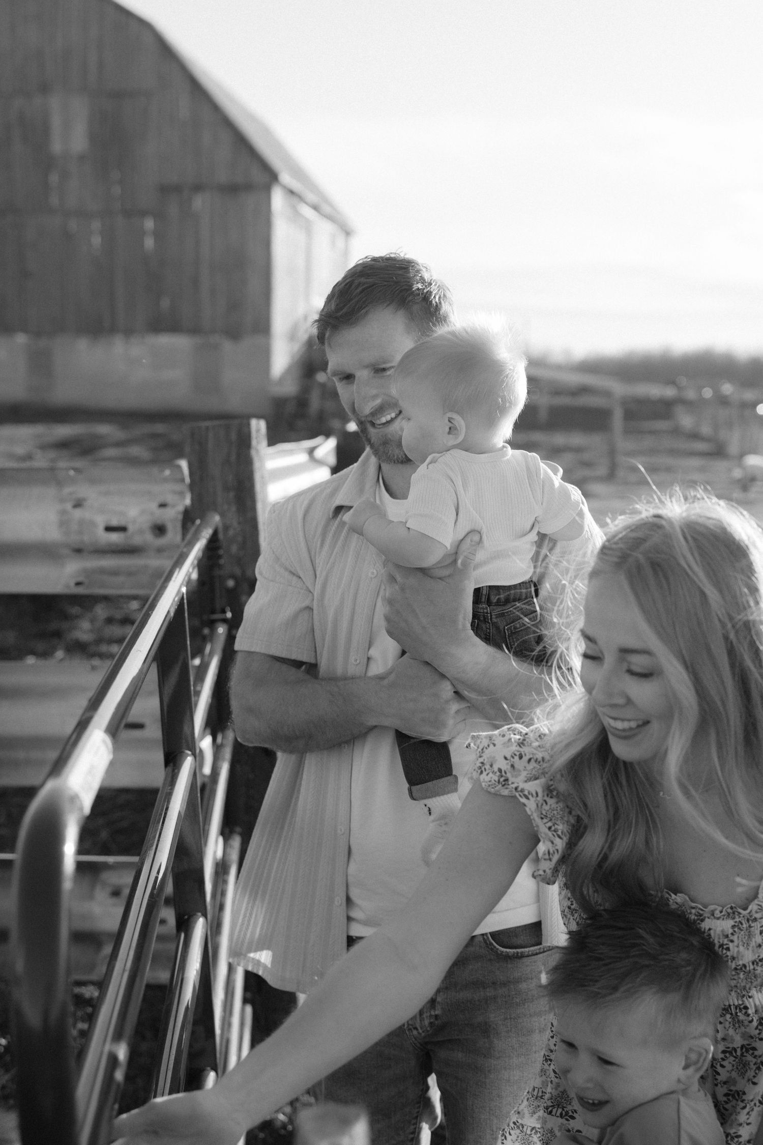 Black and white photo of a happy family with two young children near a rustic barn.