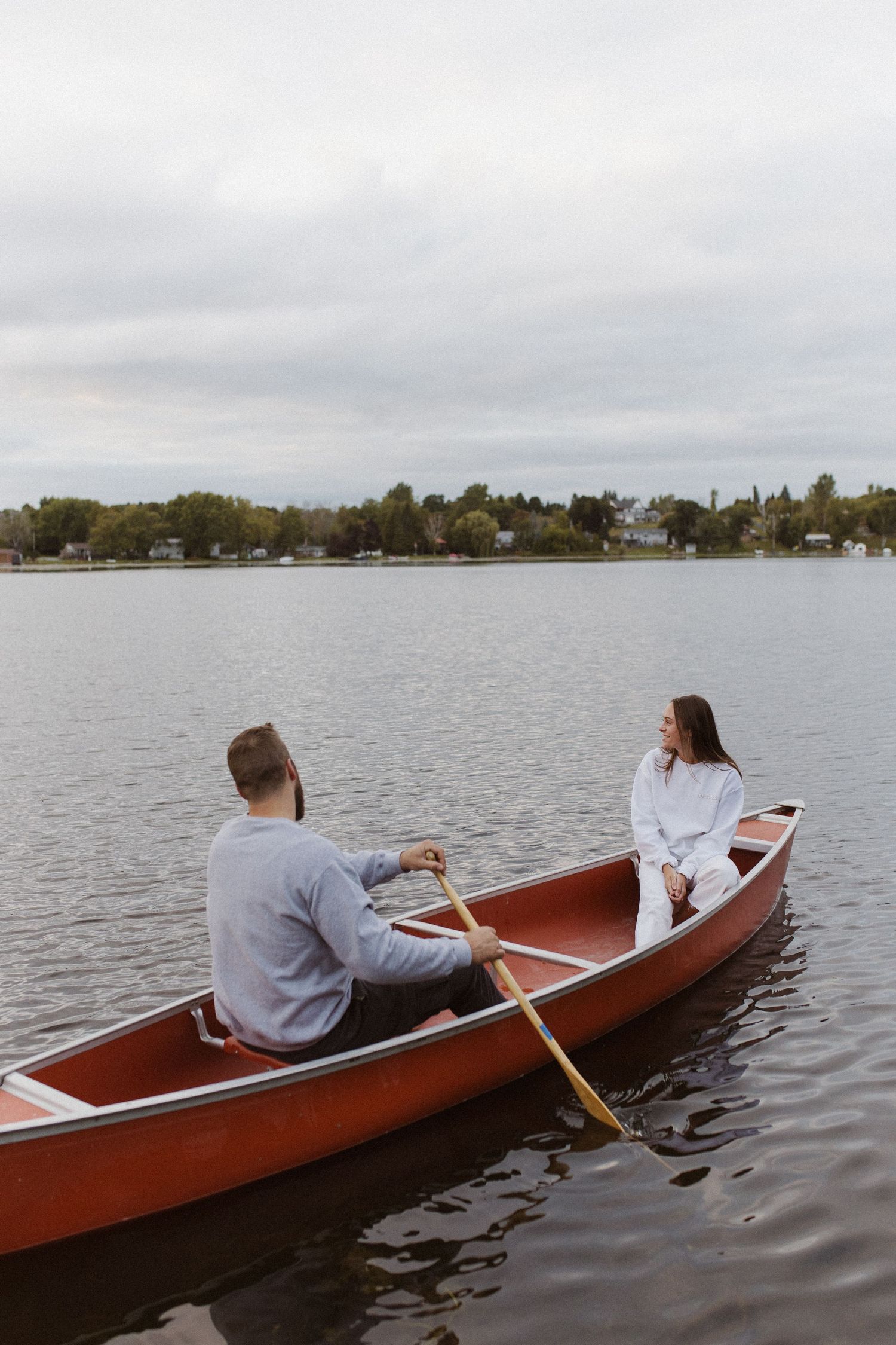 Couple sharing a quiet moment while rowing a red canoe on a calm lake.