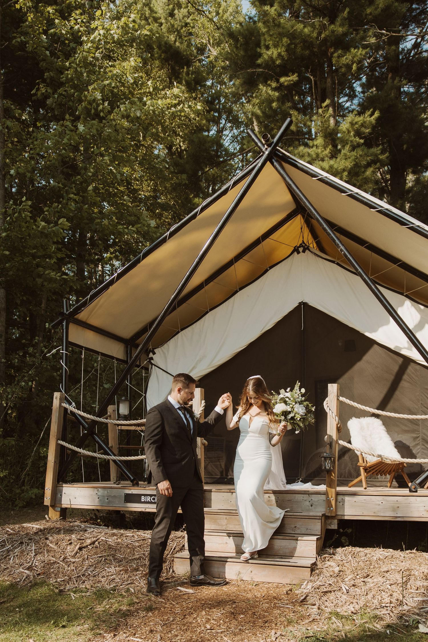 Bride and groom sharing a first dance moment on the deck of a glamping tent surrounded by tall pine trees.