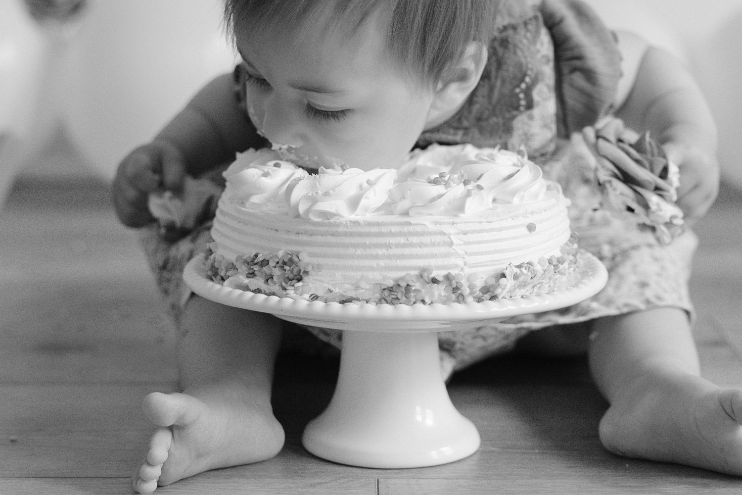 Baby eating birthday cake directly off a white pedestal cake stand.