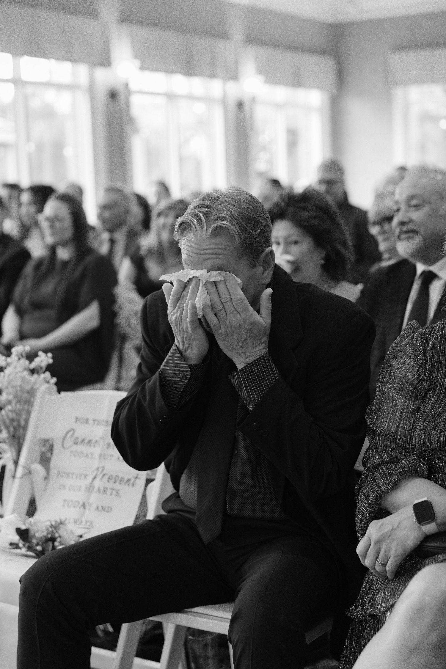 Emotional wedding guest crying into handkerchief during ceremony, black and white photo.