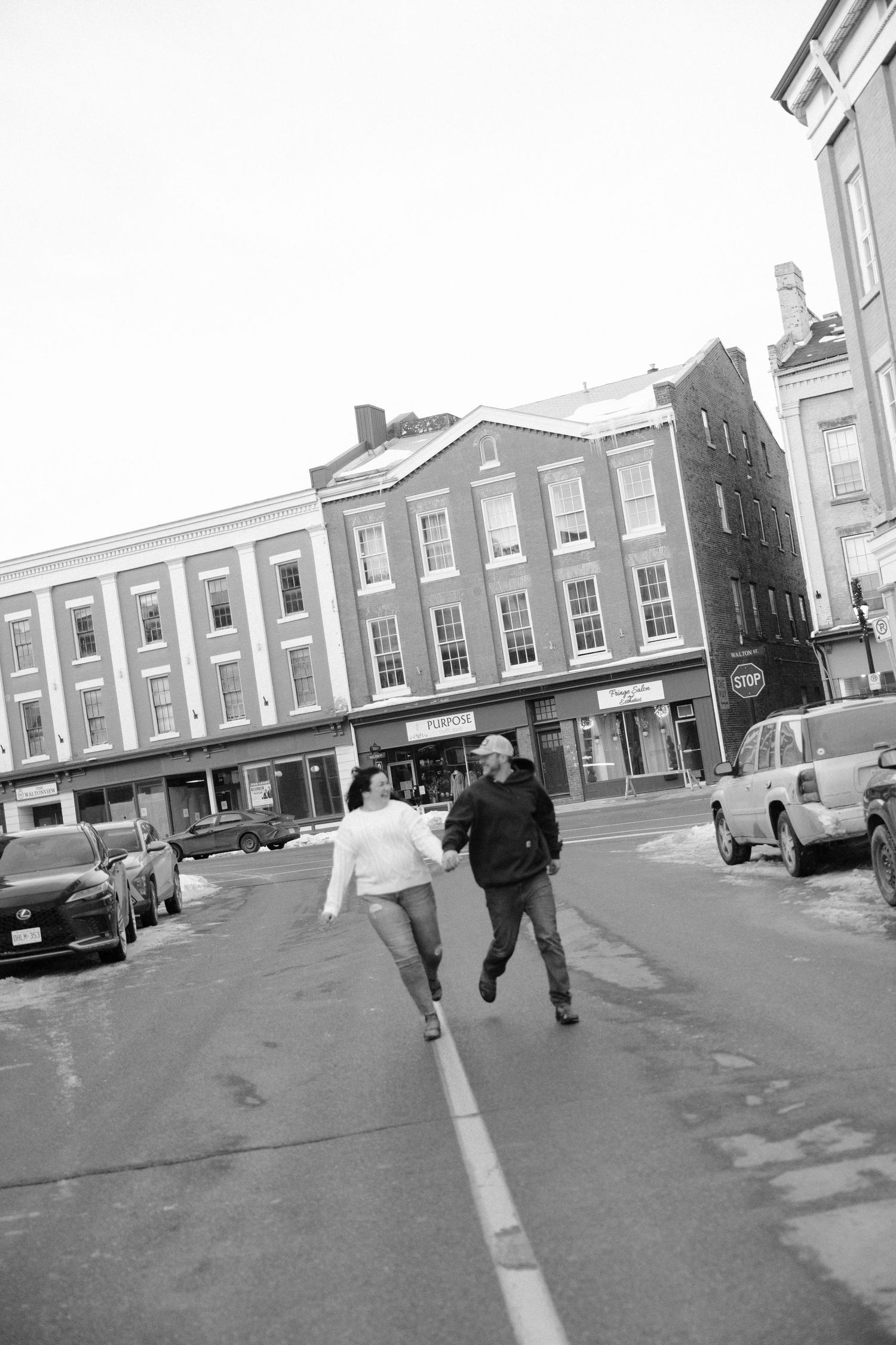 Black and white photo of a couple holding hands running across a street in a historic downtown area.