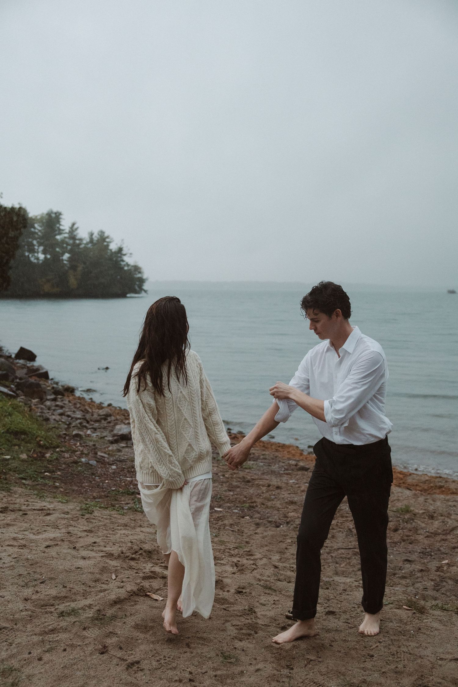 Couple dancing barefoot on sandy beach shore on a cloudy overcast day.