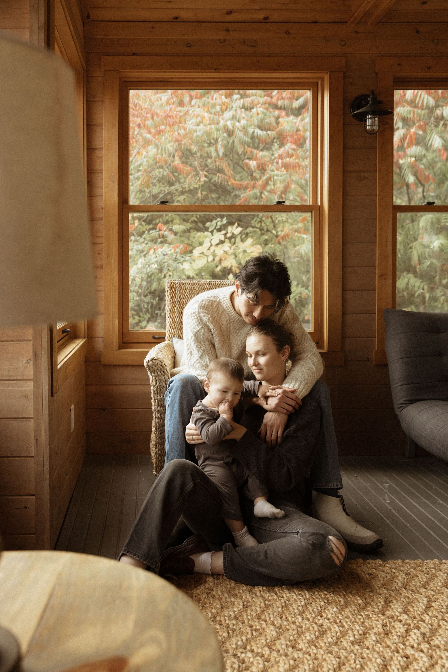 Family of three sitting together in cozy wooden cabin by autumn window.