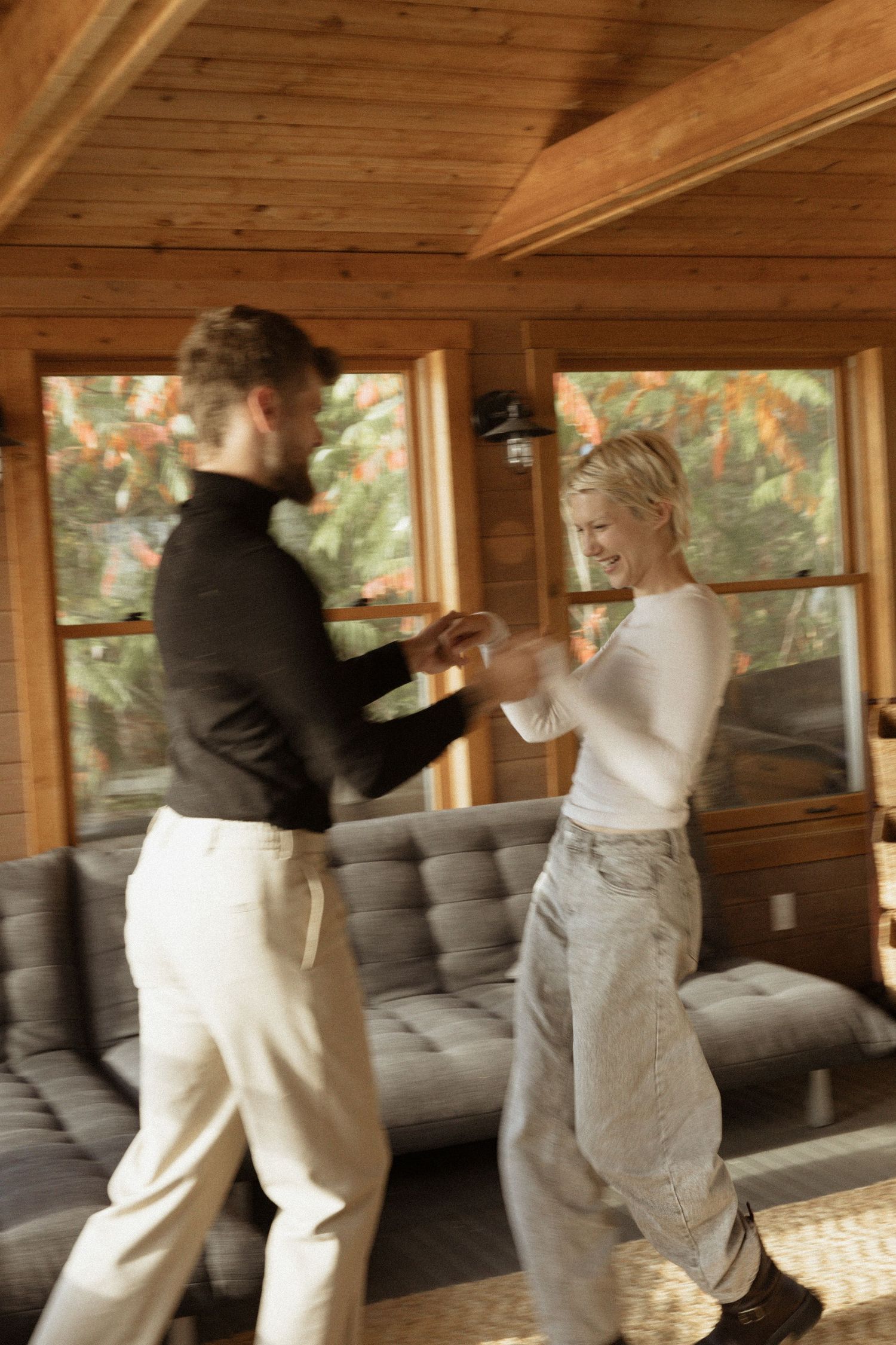 Couple dancing and smiling together in a cozy wooden cabin living room.