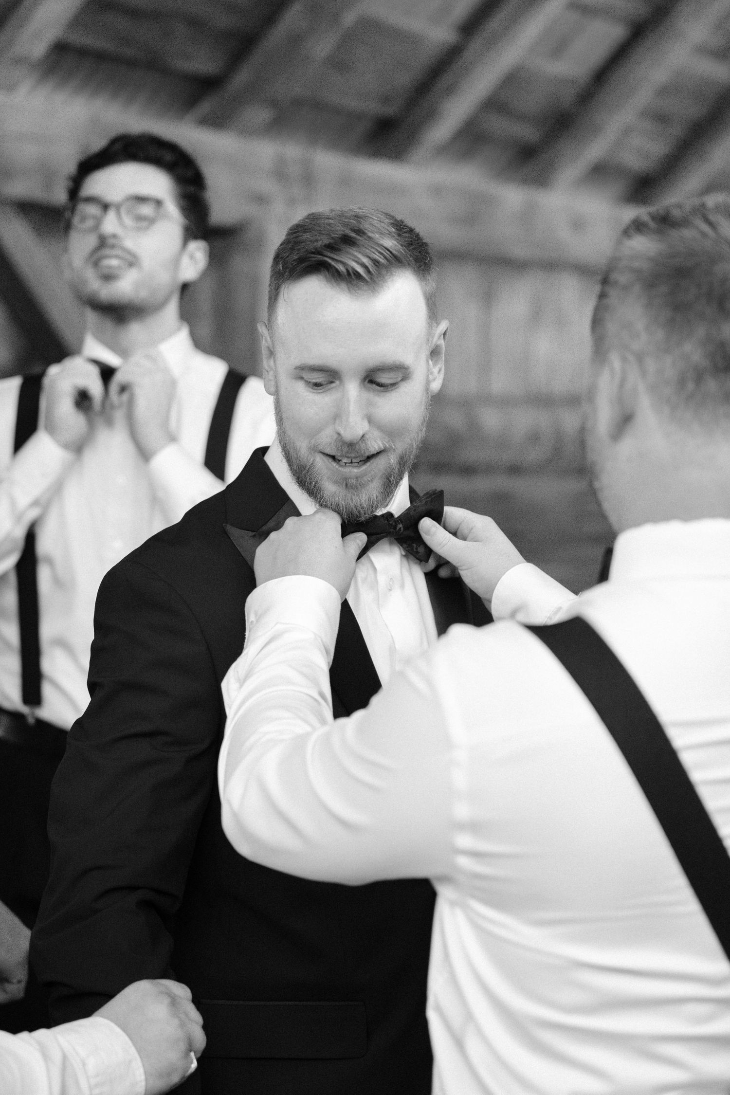 Black and white photo of groomsmen helping the groom adjust his bow tie before the wedding.