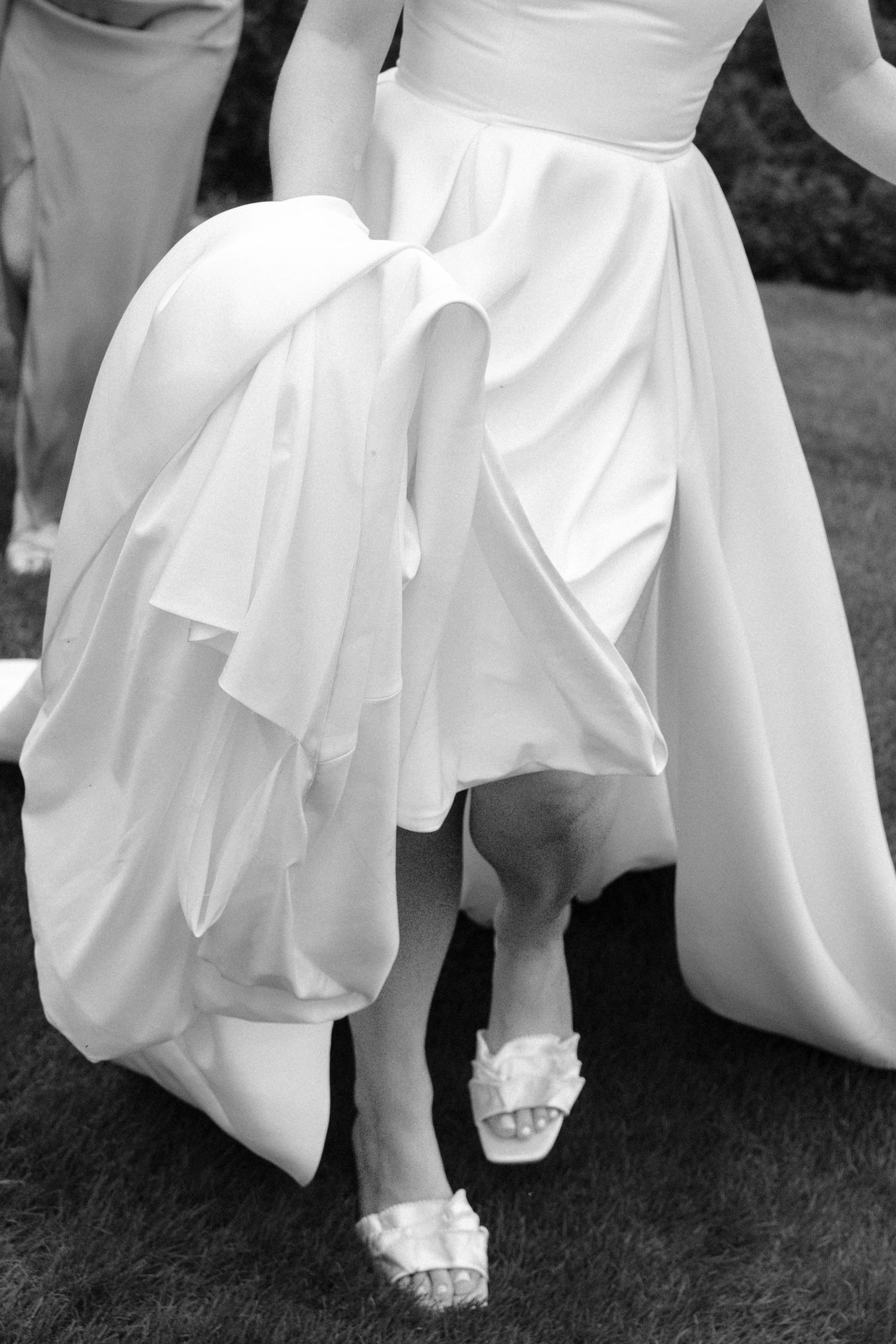 Close-up black and white photo of bride's white gown and floral heels walking.