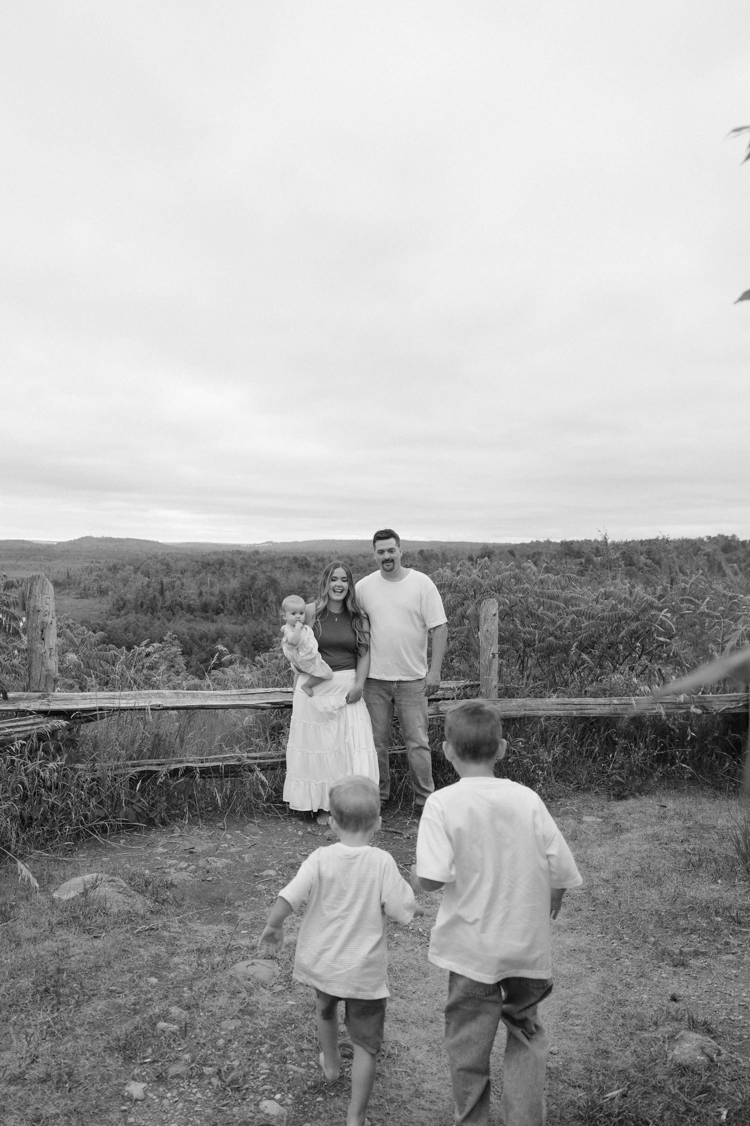 Black and white family photo of parents with baby as two boys run toward them.
