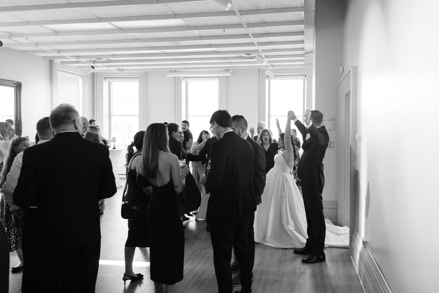 Black and white photo of wedding guests mingling and celebrating at an elegant indoor reception venue.