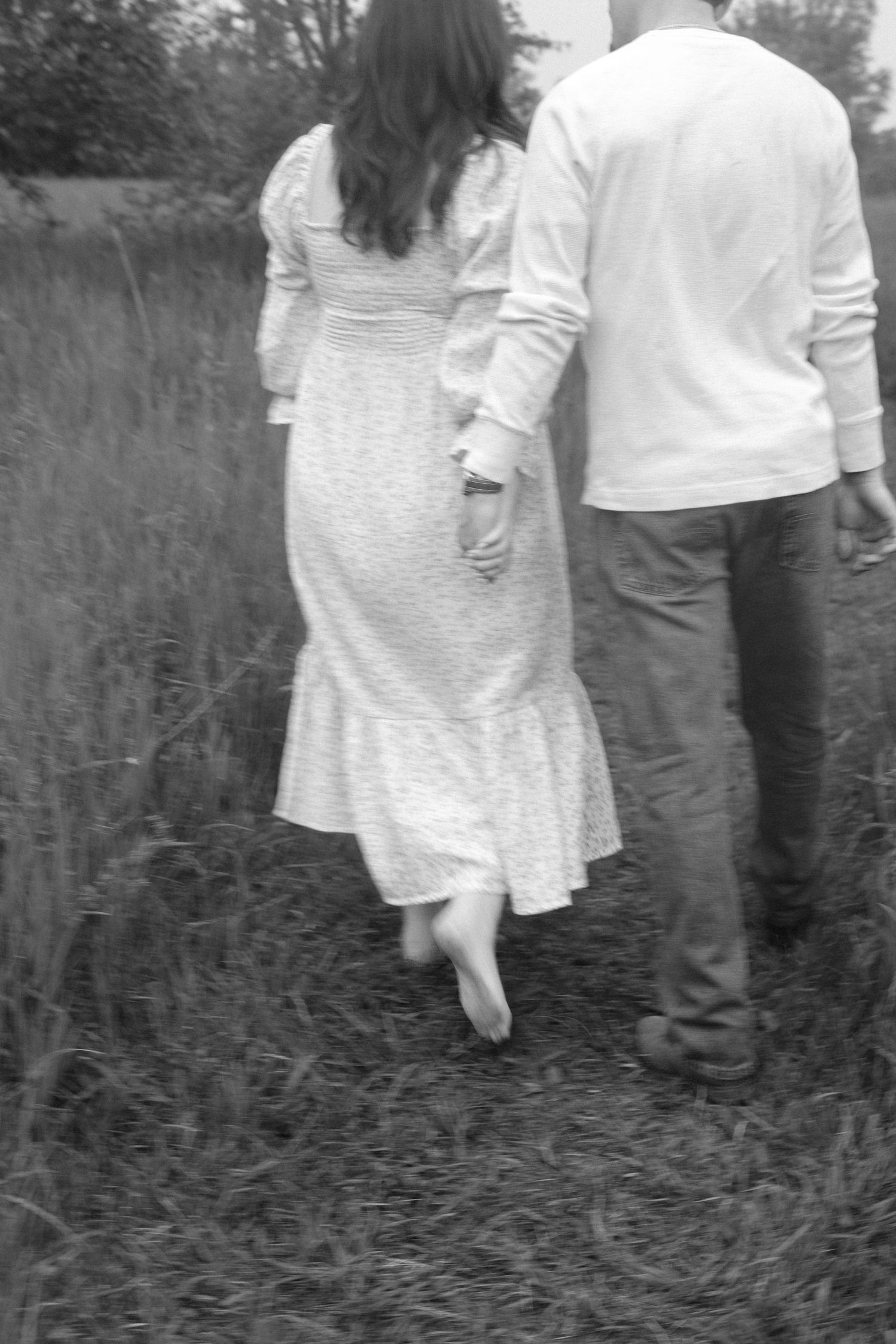 Black and white photo of couple walking hand in hand through a field.