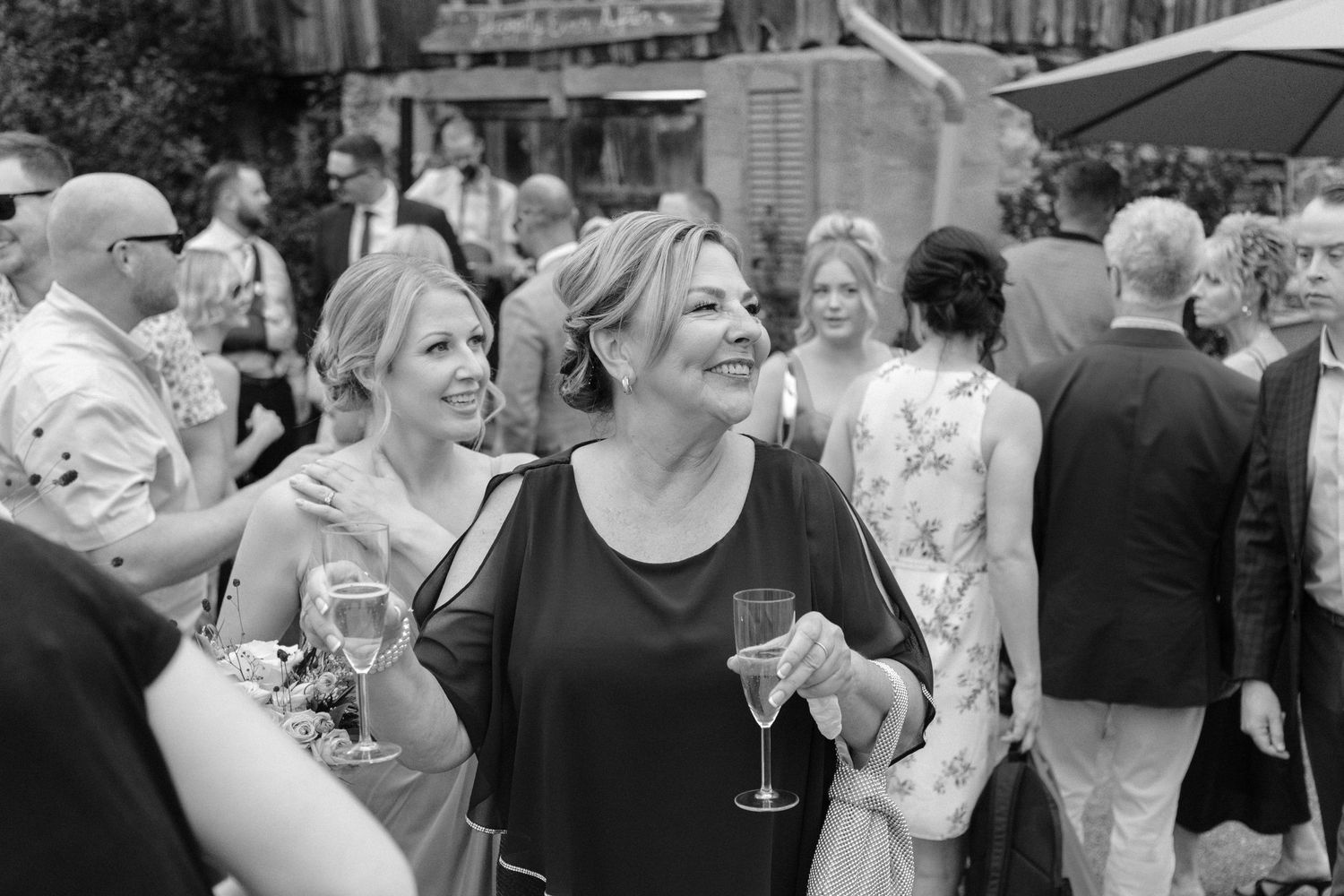 Black and white photo of smiling woman holding champagne glass socializing at an outdoor wedding reception.