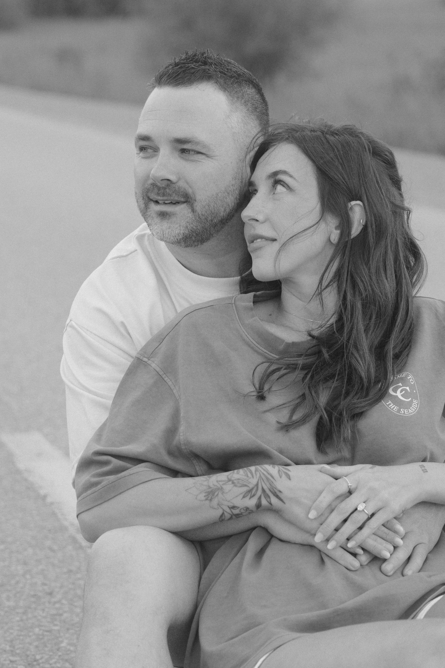 Black and white portrait of engaged couple sitting together on road embracing.
