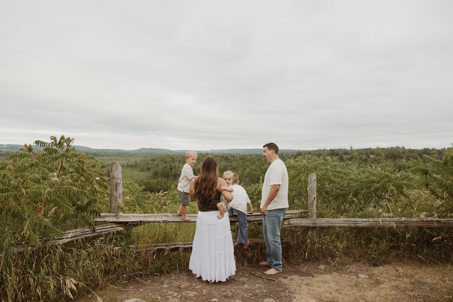 Family of four standing on a wooden overlook surrounded by lush green countryside on a cloudy day.