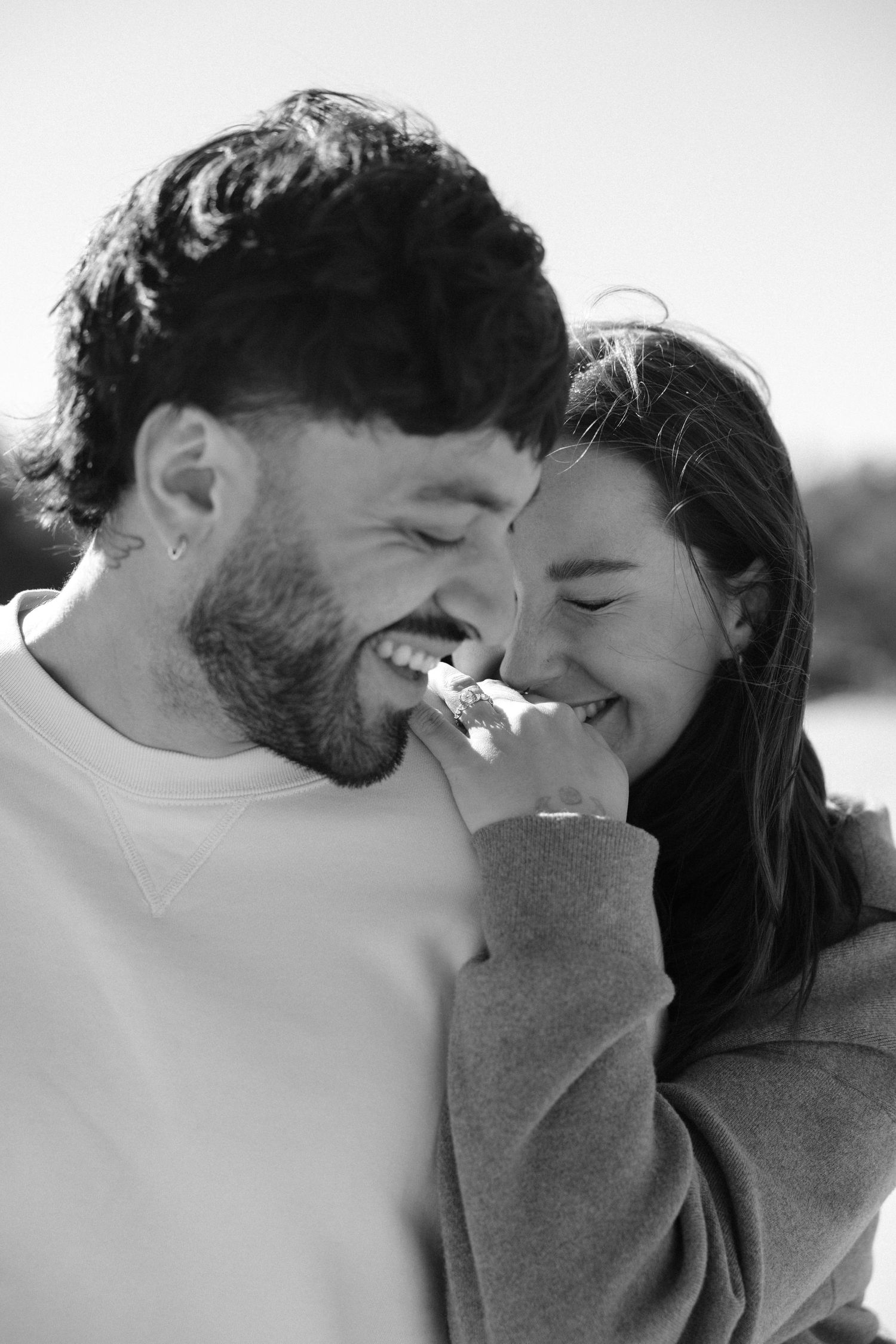 Happy couple laughing together in a joyful black and white engagement portrait outdoors.