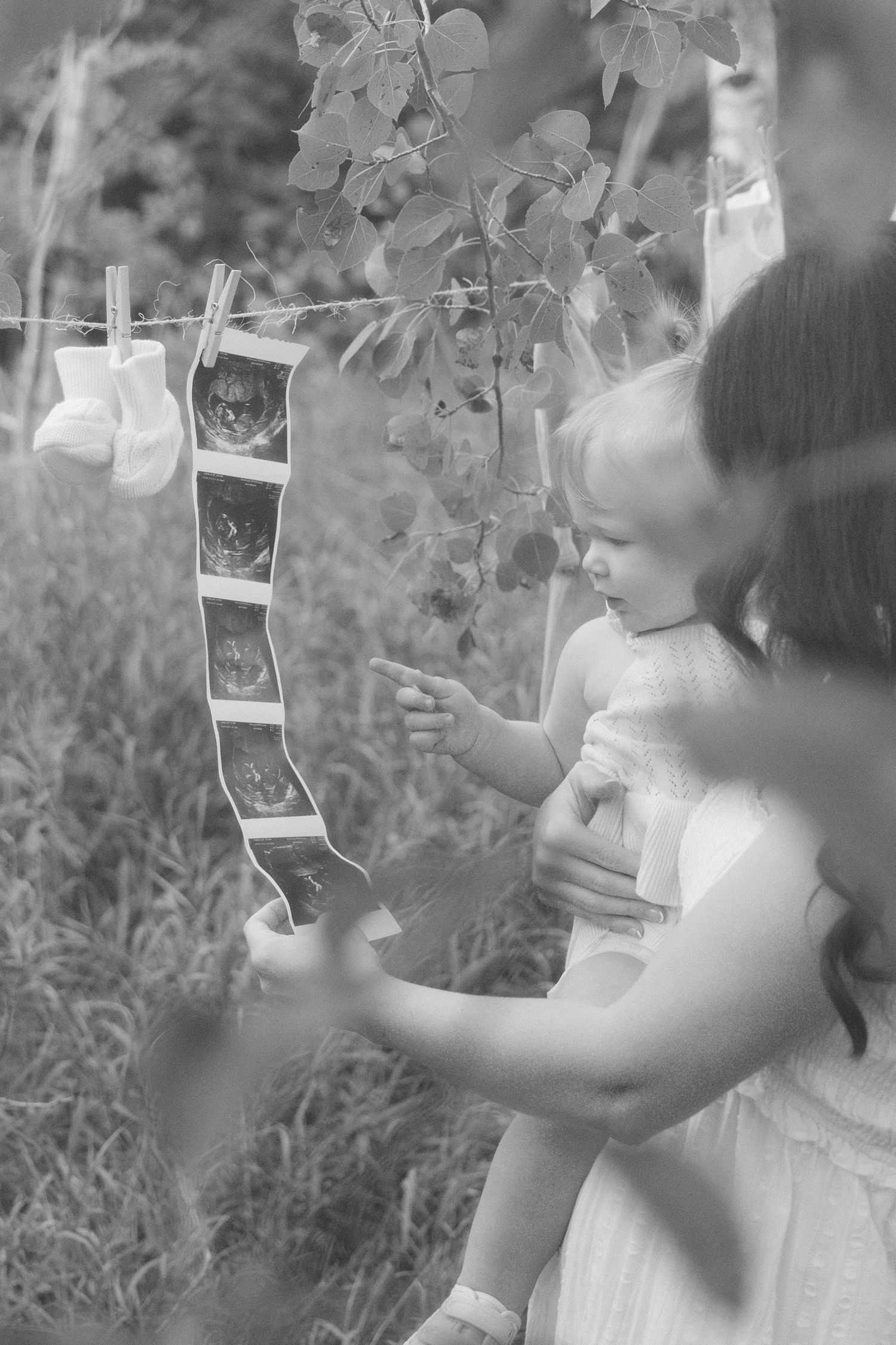 Black and white photo of a mother holding a toddler looking at ultrasound photos.
