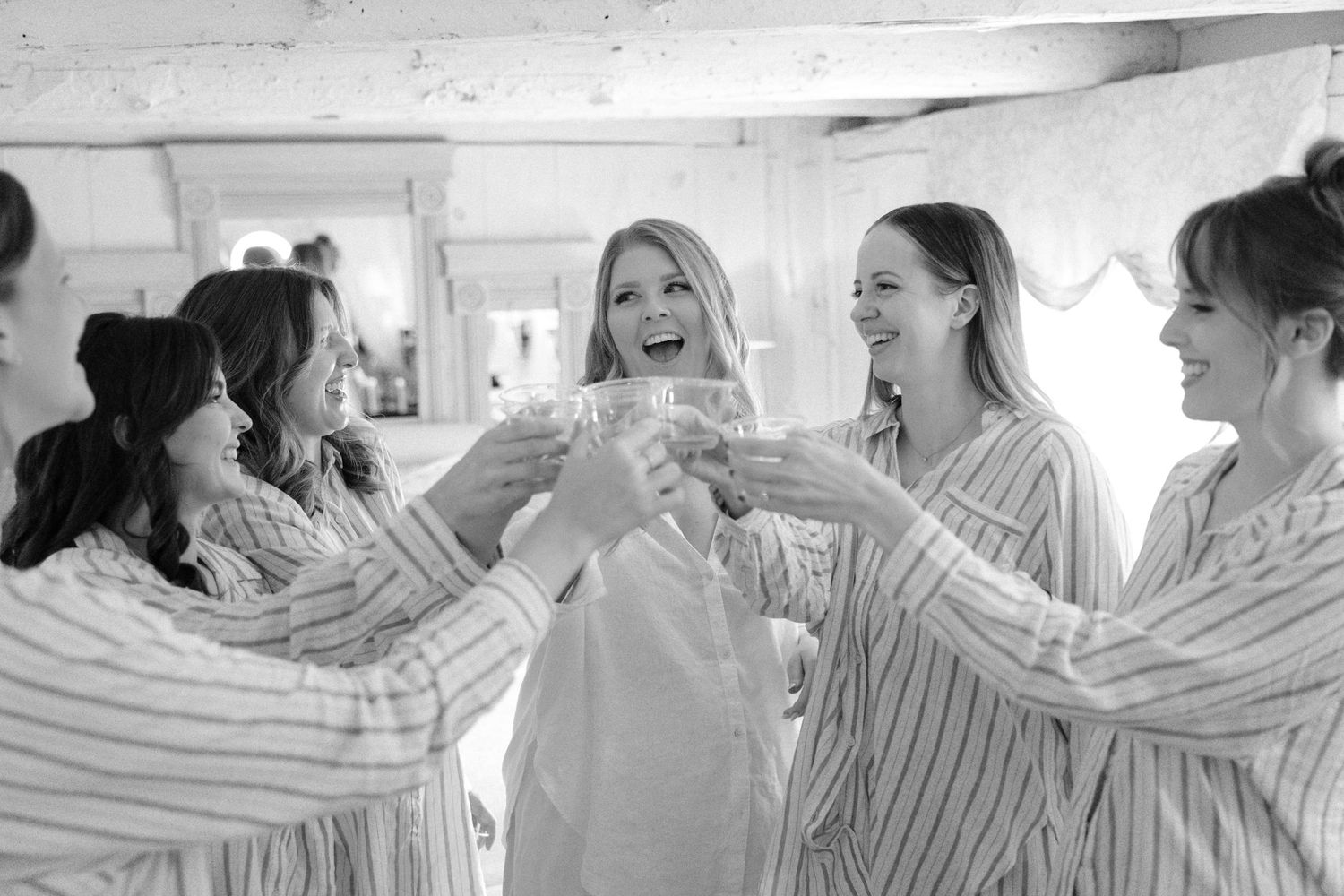 Black and white photo of bride and bridesmaids in striped robes toasting with champagne.