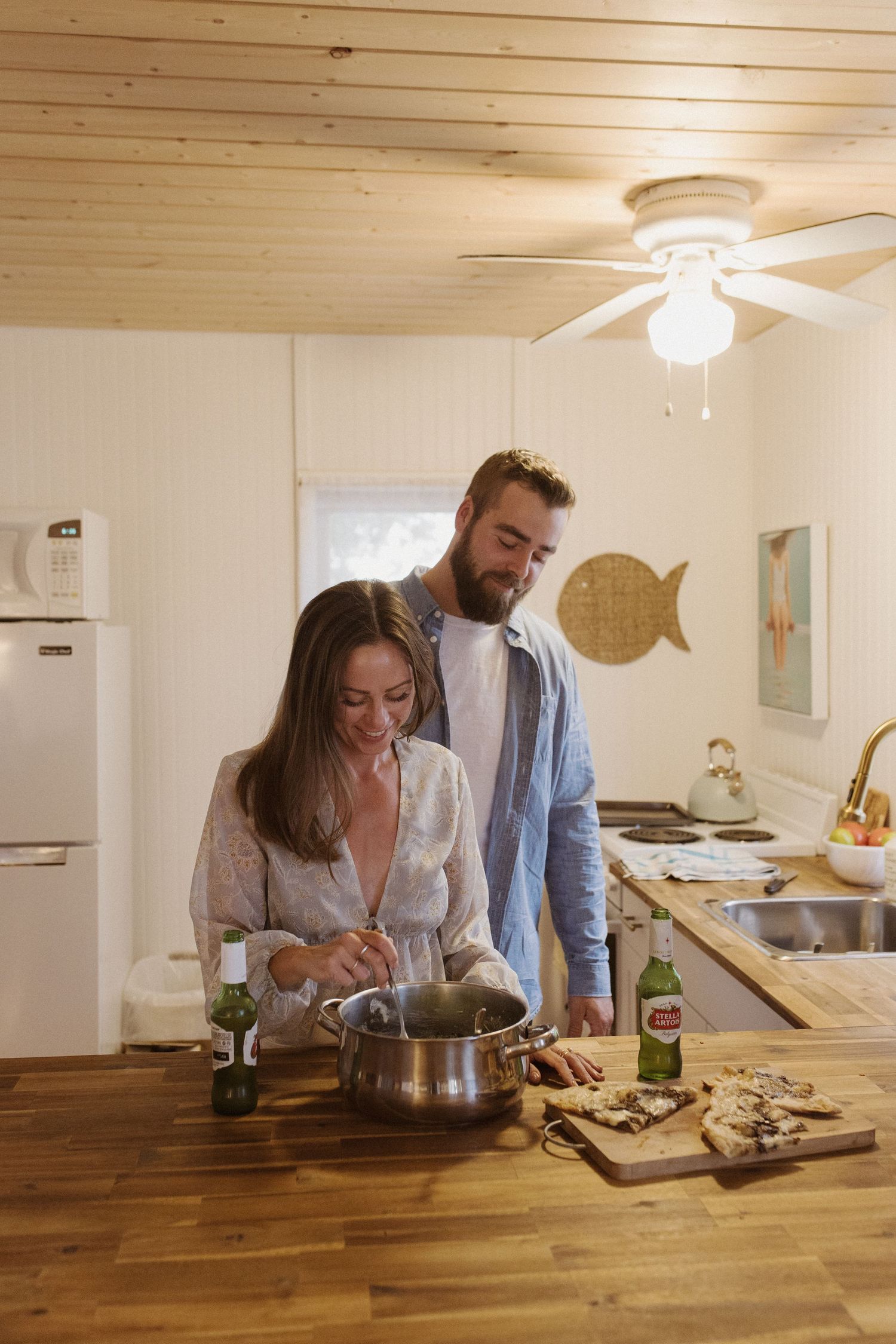 Couple cooking together in a cozy wooden kitchen with beer bottles on the counter.