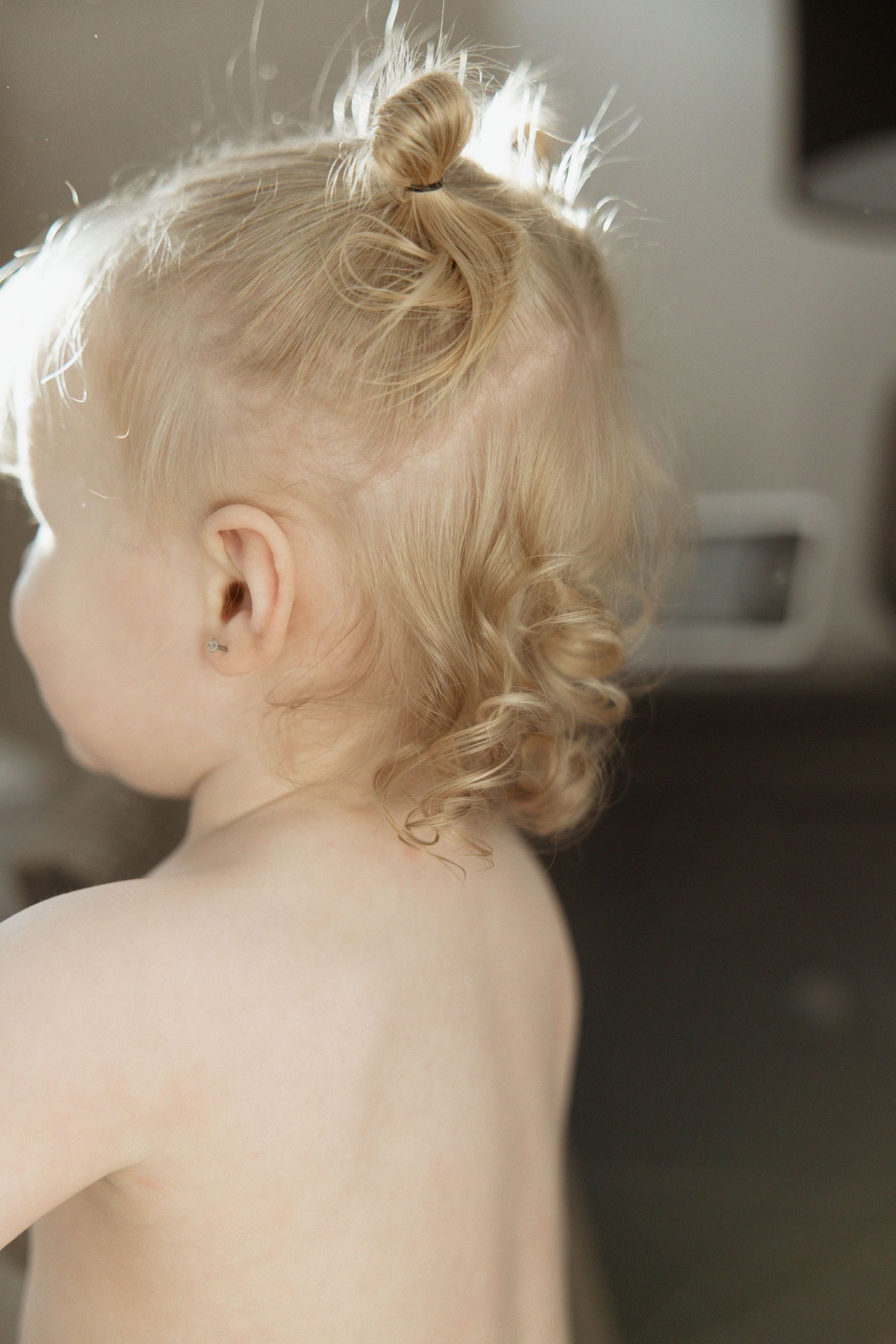 Close-up of a blonde toddler with a tiny bun hairstyle, soft natural lighting highlighting curly hair.
