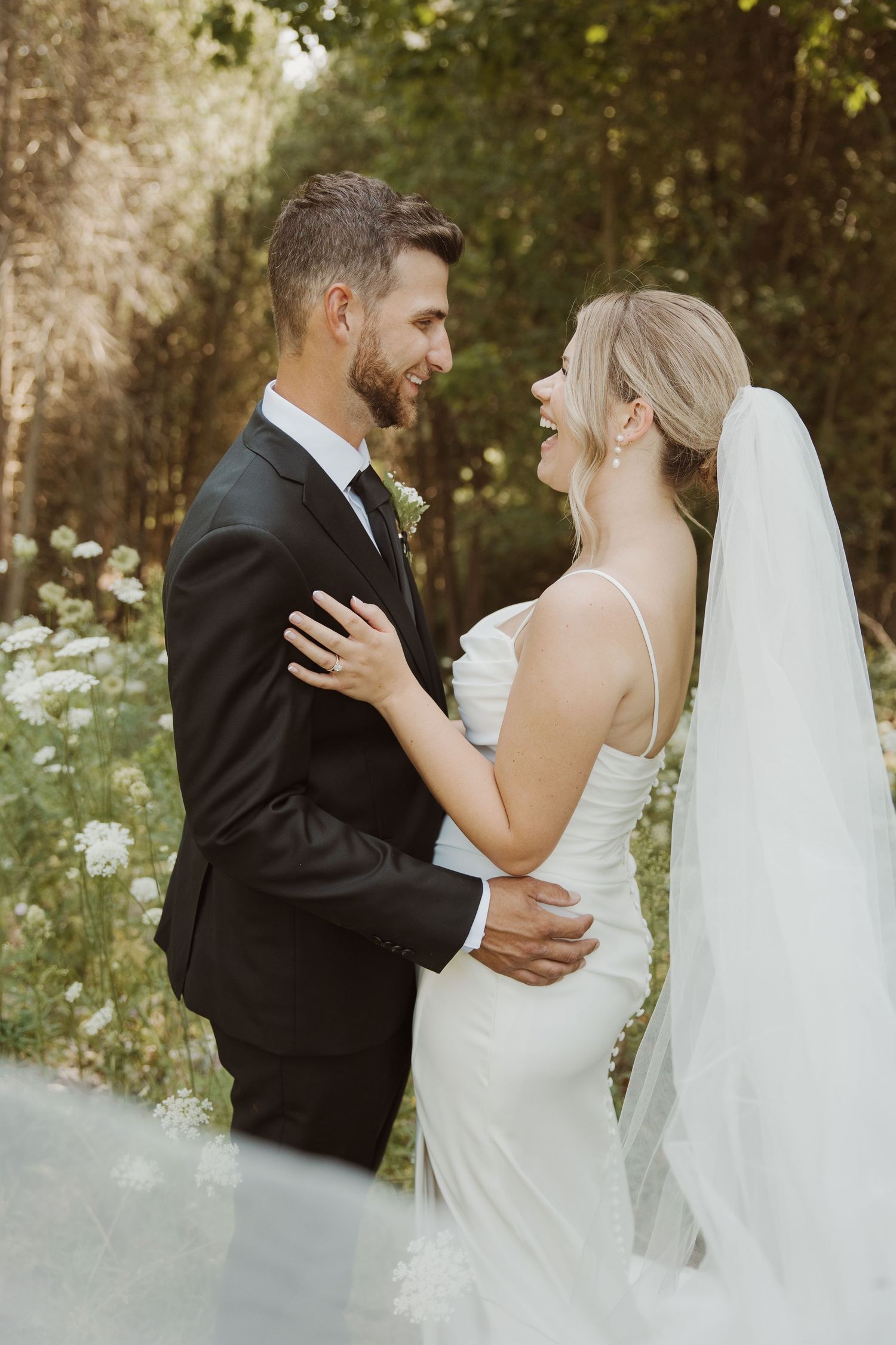Smiling bride and groom embrace in a lush forest setting on their wedding day.