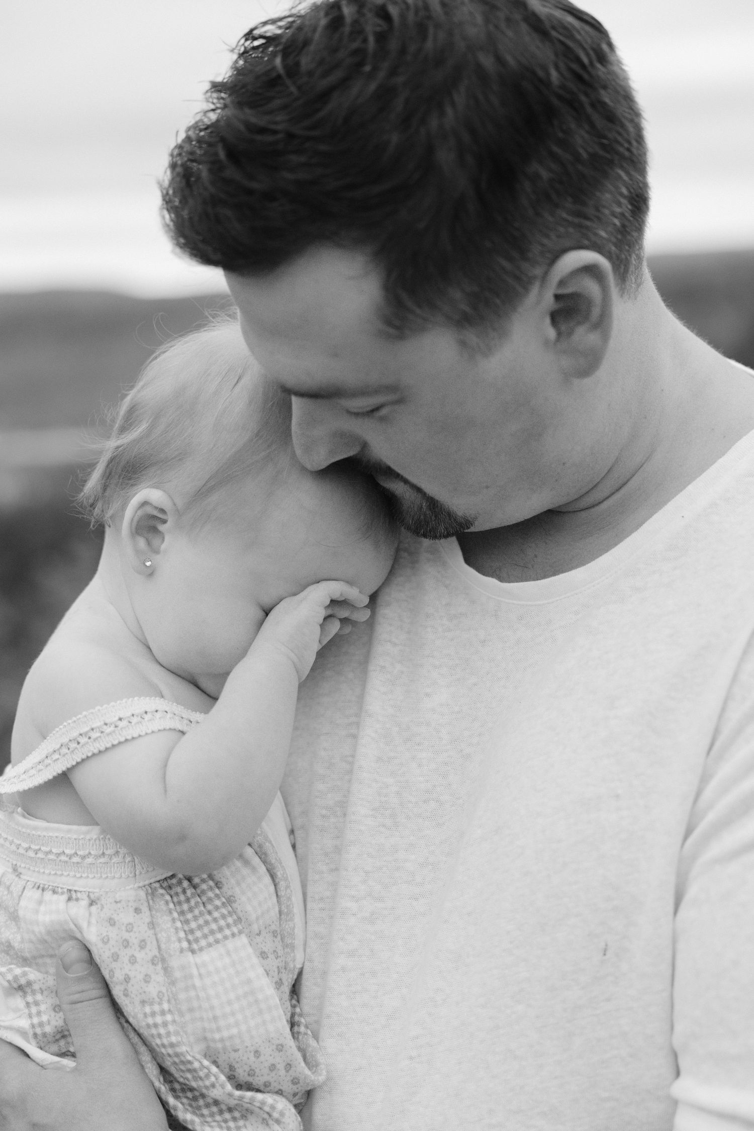 Black and white photo of a father tenderly holding and nuzzling his baby outdoors.