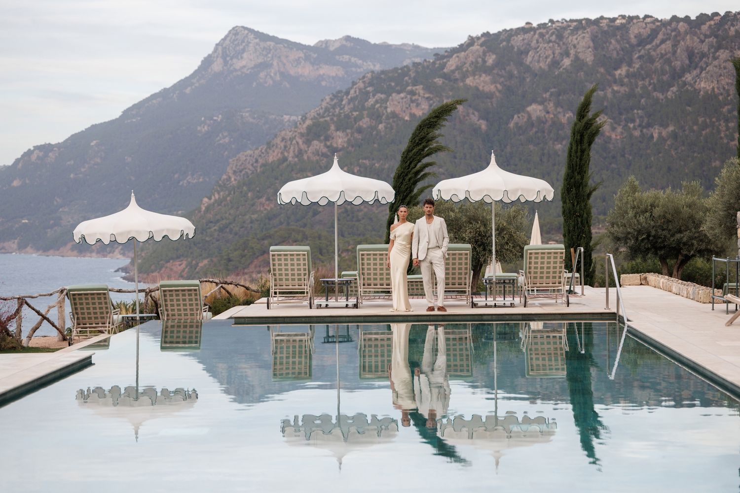 Scenic mountain poolside with white umbrellas and lounge chairs overlooking coastal view. Mallorca Son Bunyola