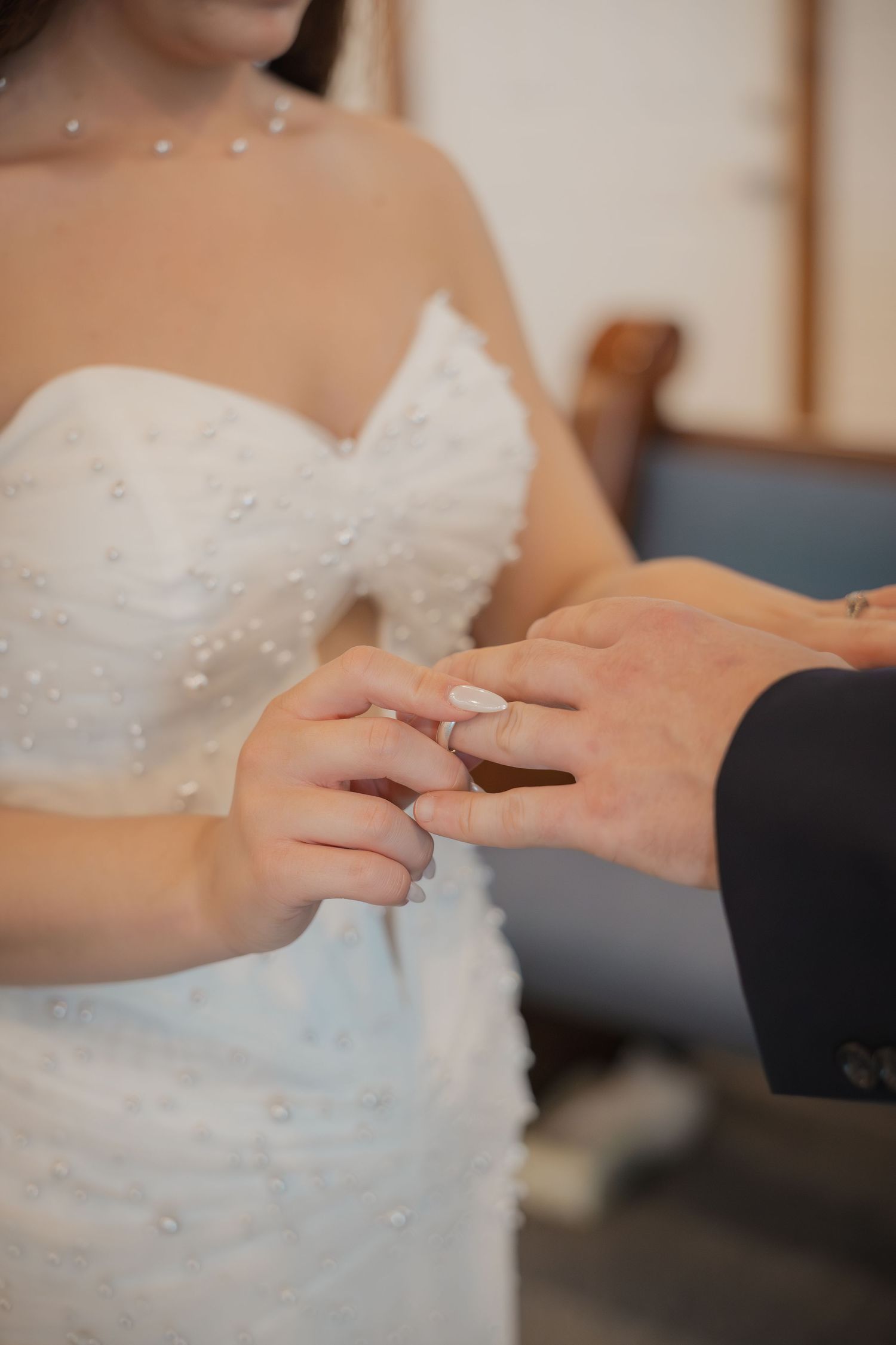 Bride in pearl-embellished white gown placing a wedding ring on groom's finger during ceremony.