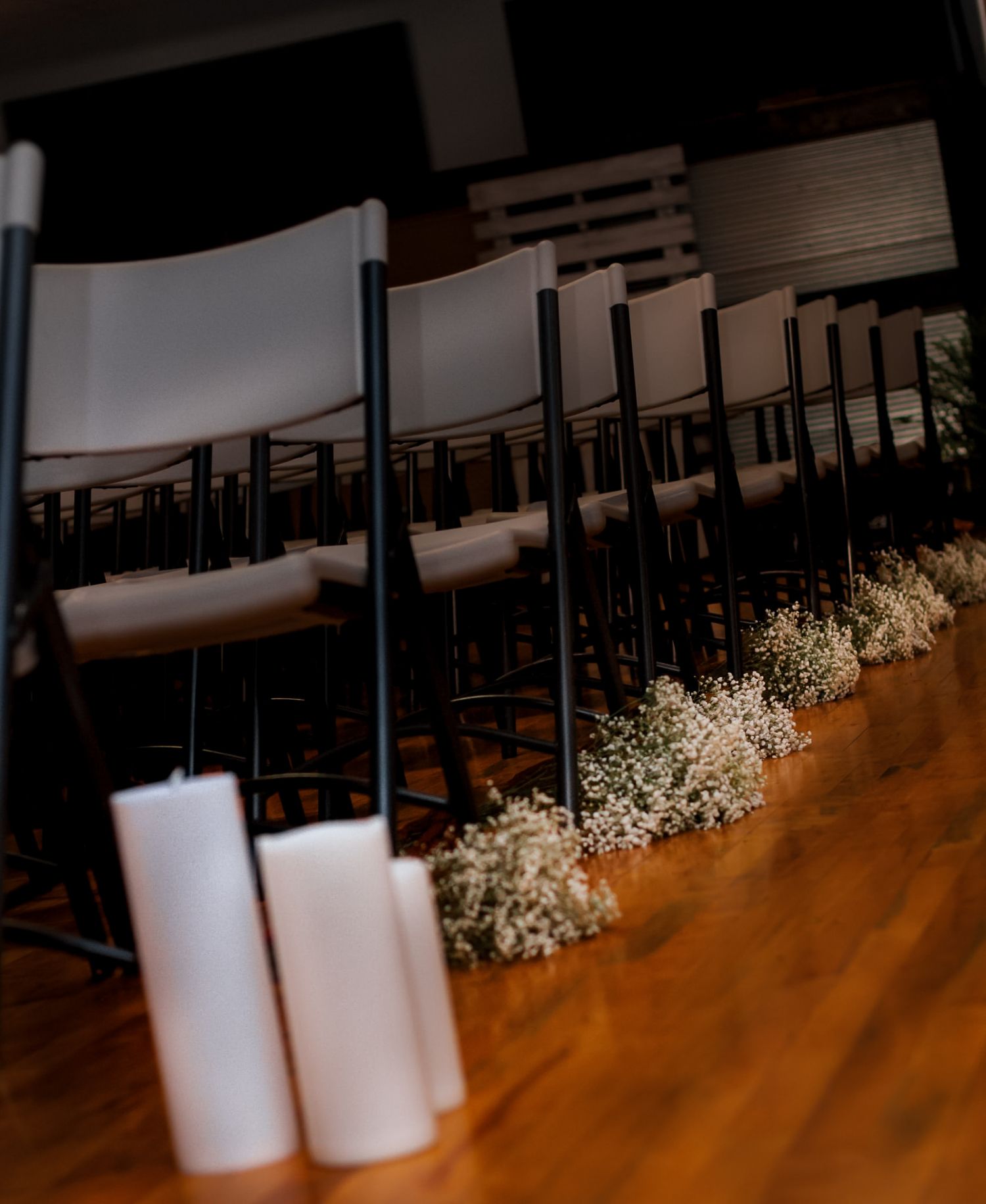 Elegant wedding ceremony aisle with white pillar candles, baby's breath flowers, and rows of dark folding chairs.