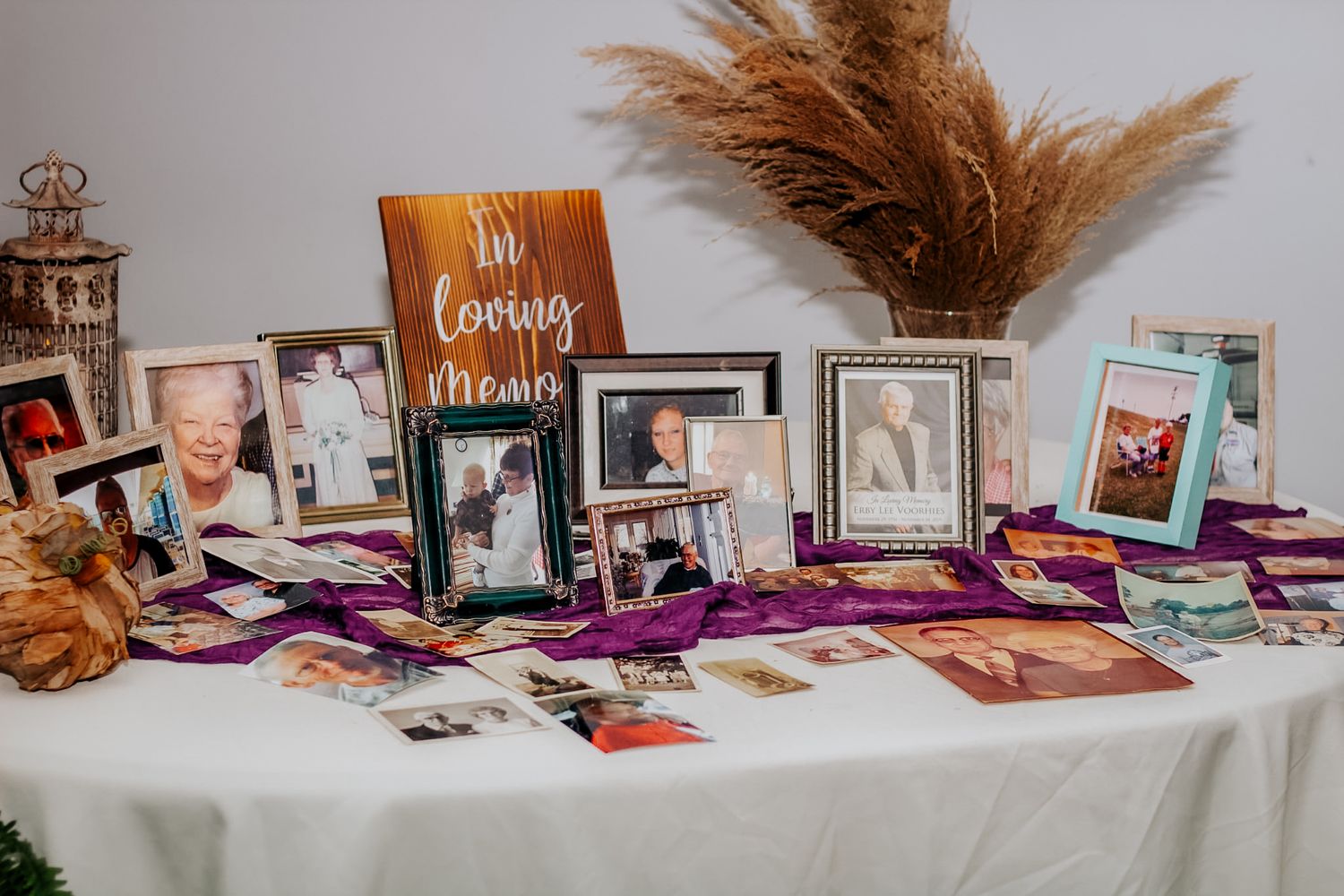 A memorial table display with framed photos and an In Loving Memory sign on a purple cloth at a funeral reception.
