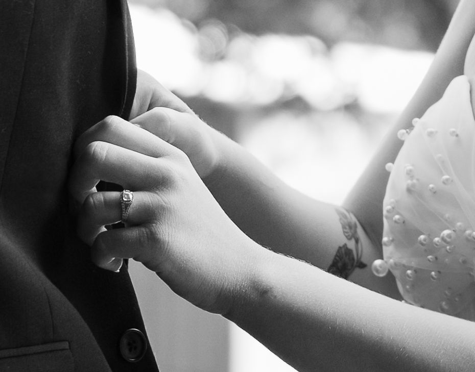 Black and white closeup of bride and groom holding hands with wedding ring detail.