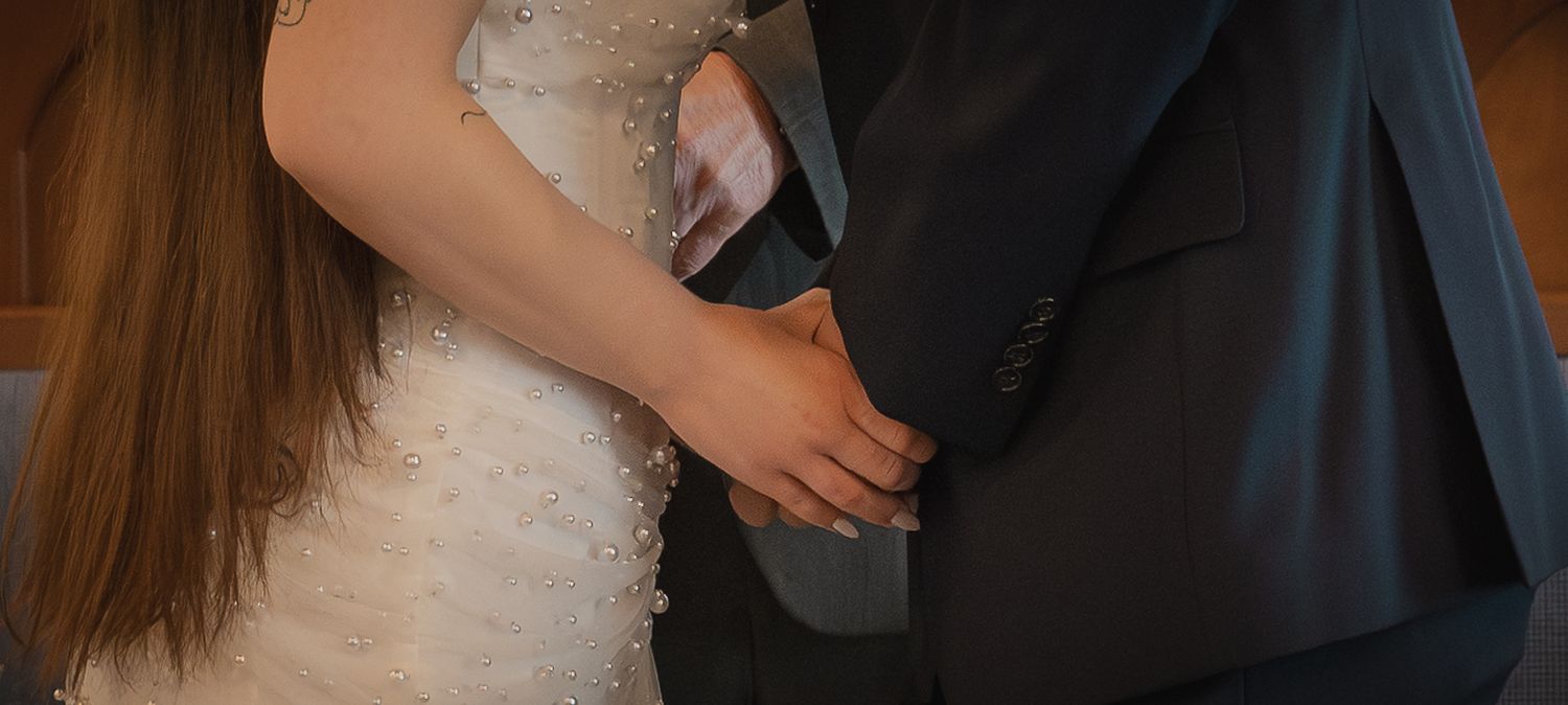 Bride in white lace wedding dress holding hands with groom in dark suit during wedding ceremony.