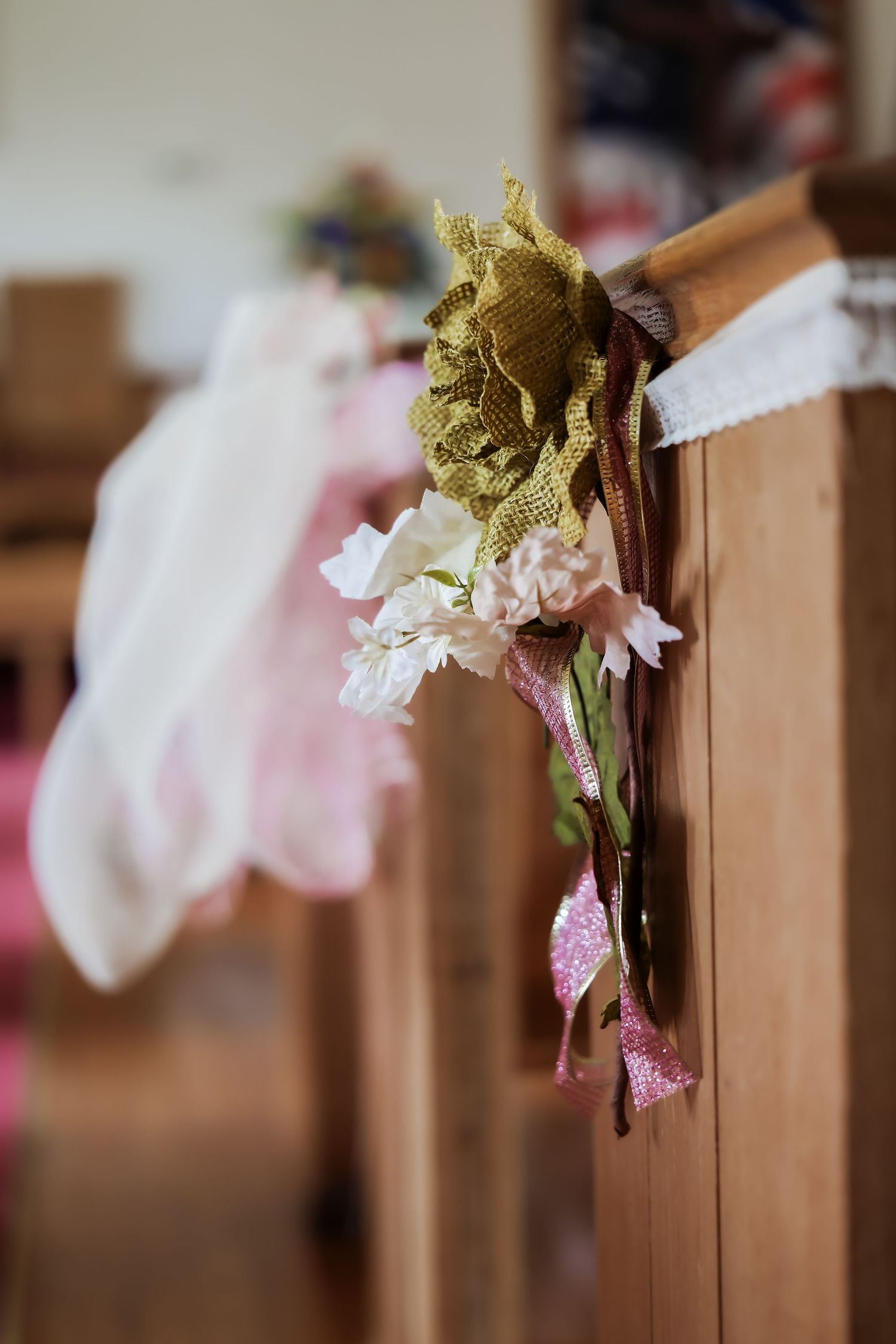 Rustic wedding pew decoration with burlap bow, pink and white flowers, and ribbon accents on wooden church bench.