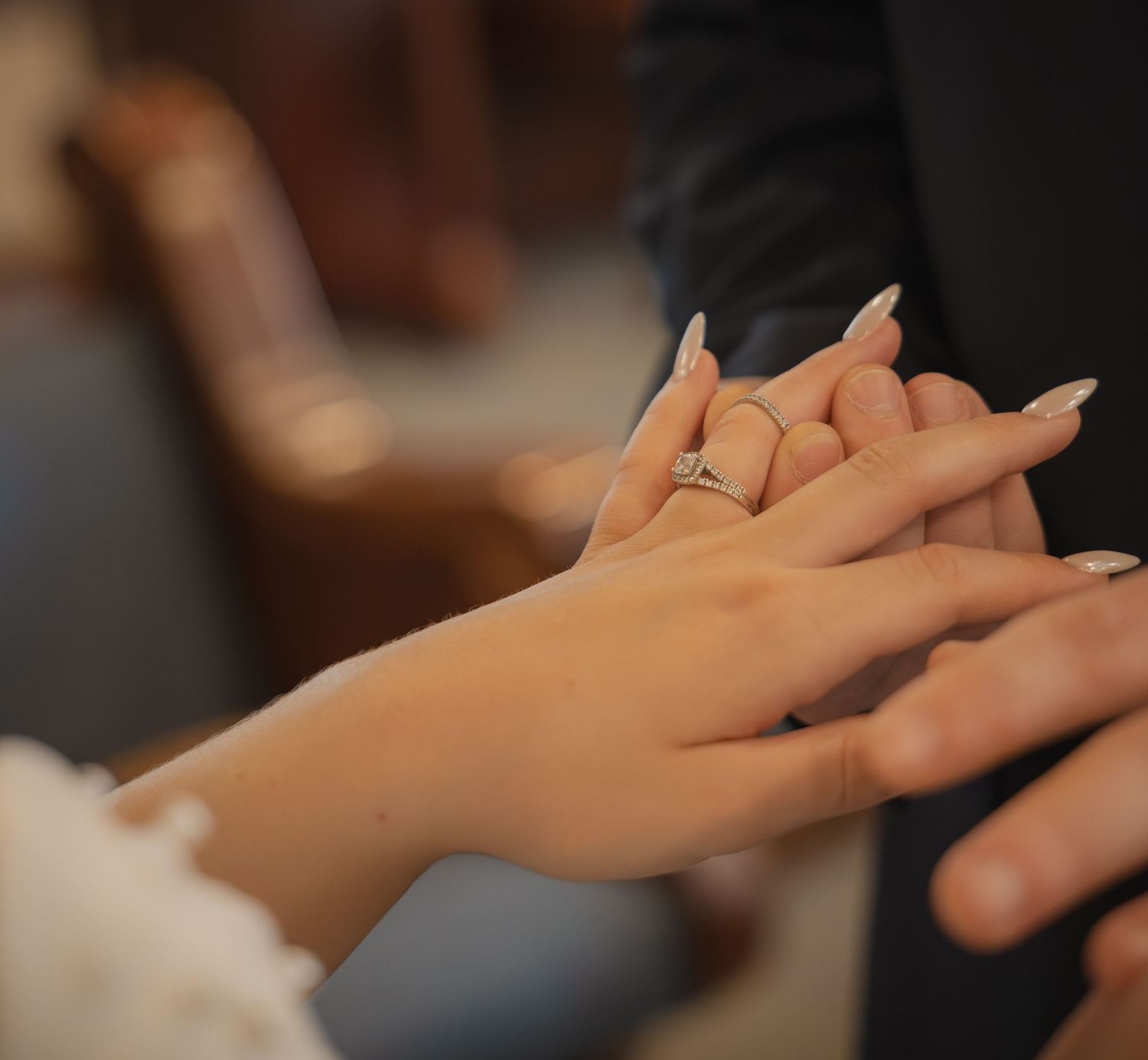 Groom placing diamond engagement ring on brides hand during wedding ceremony closeup.
