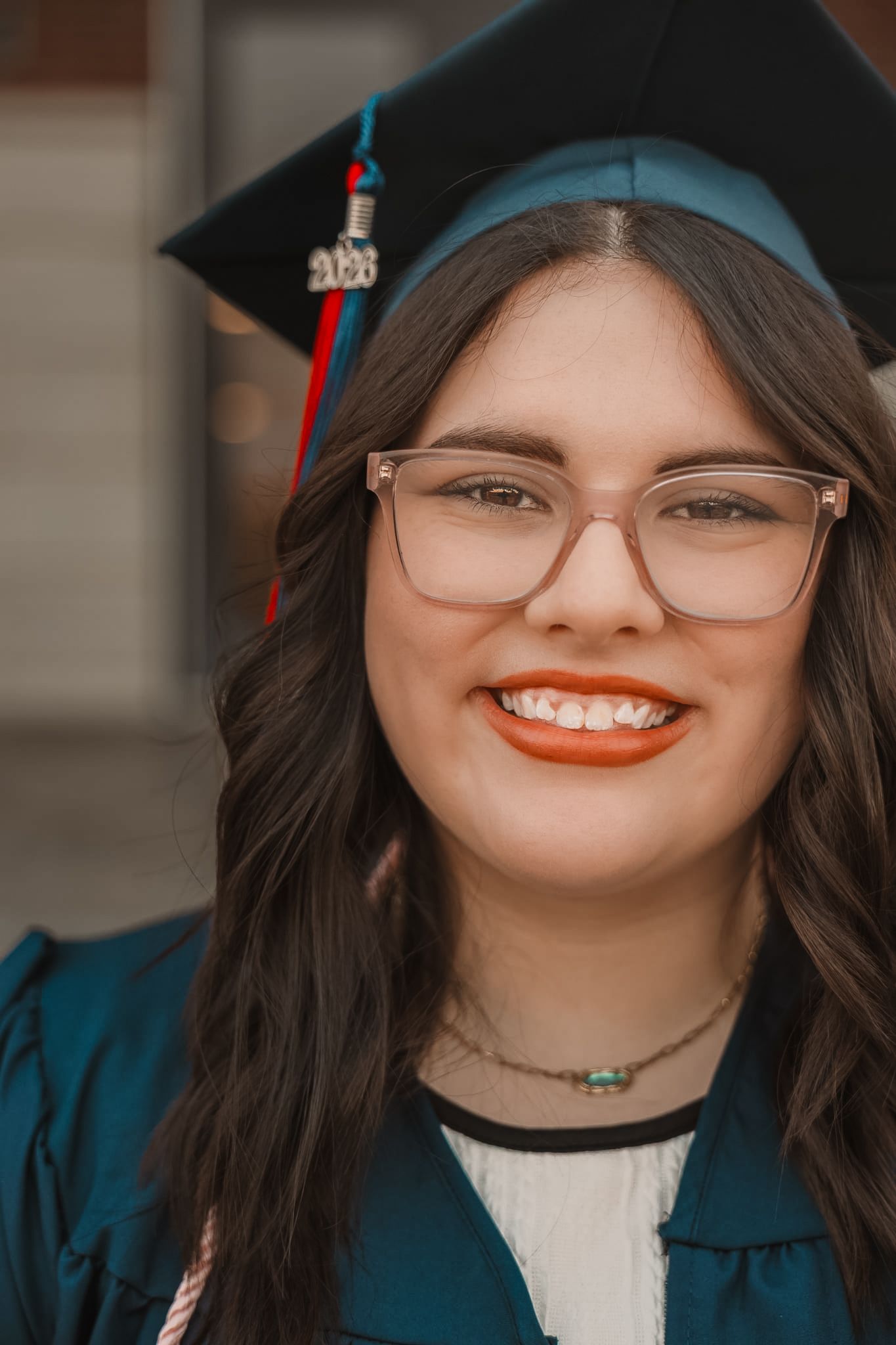 Smiling young woman in teal graduation gown and cap with glasses celebrating her academic achievement.