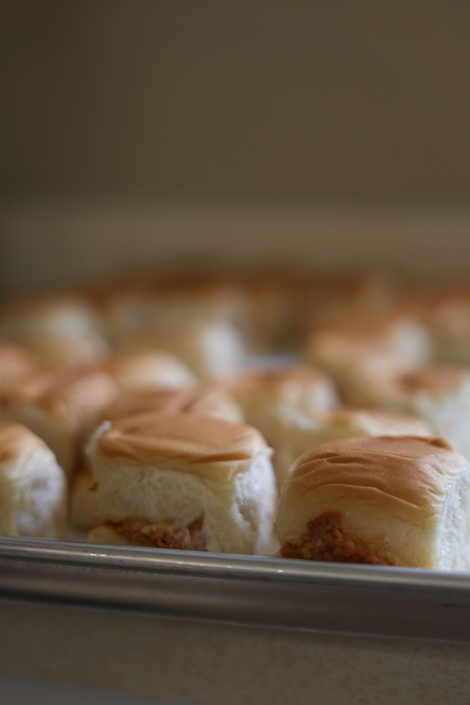 Freshly baked soft dinner rolls golden brown on top arranged in a silver baking pan.