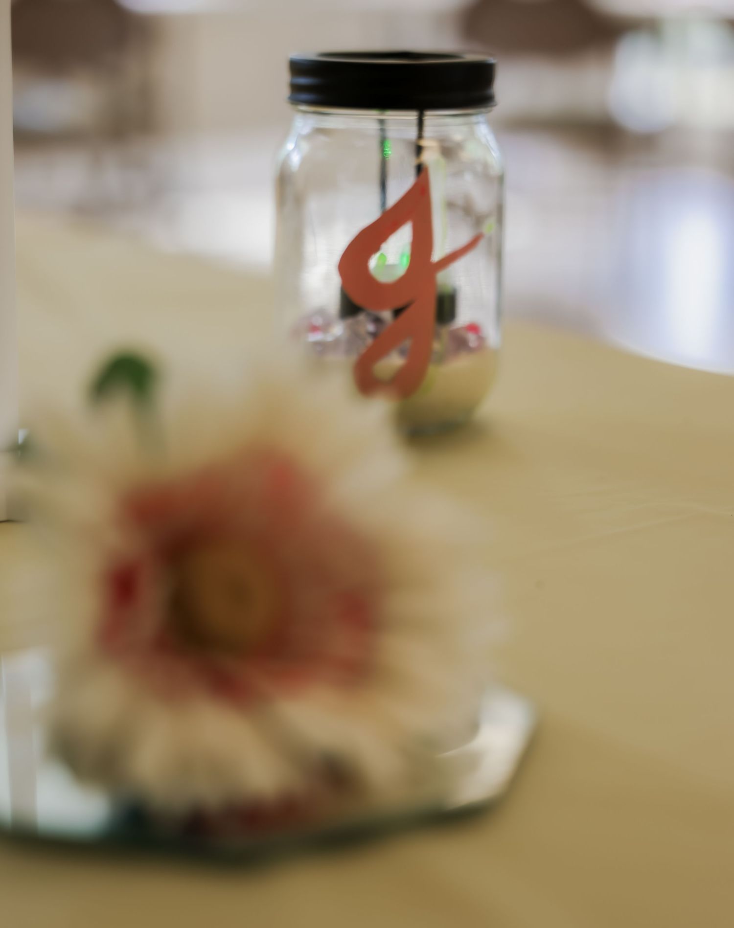Mason jar centerpiece with red monogram letter on table with blurred pink gerbera daisy in foreground.
