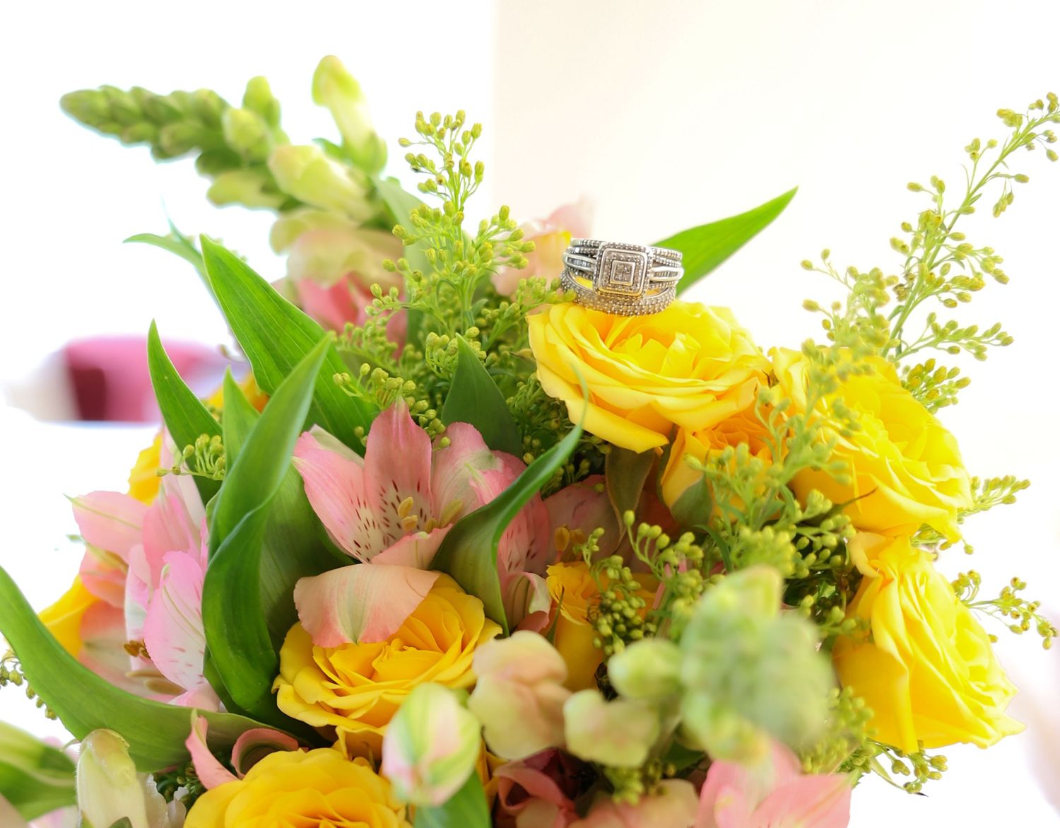 Diamond engagement ring displayed on a colorful bouquet of yellow roses and pink flowers for a wedding celebration.